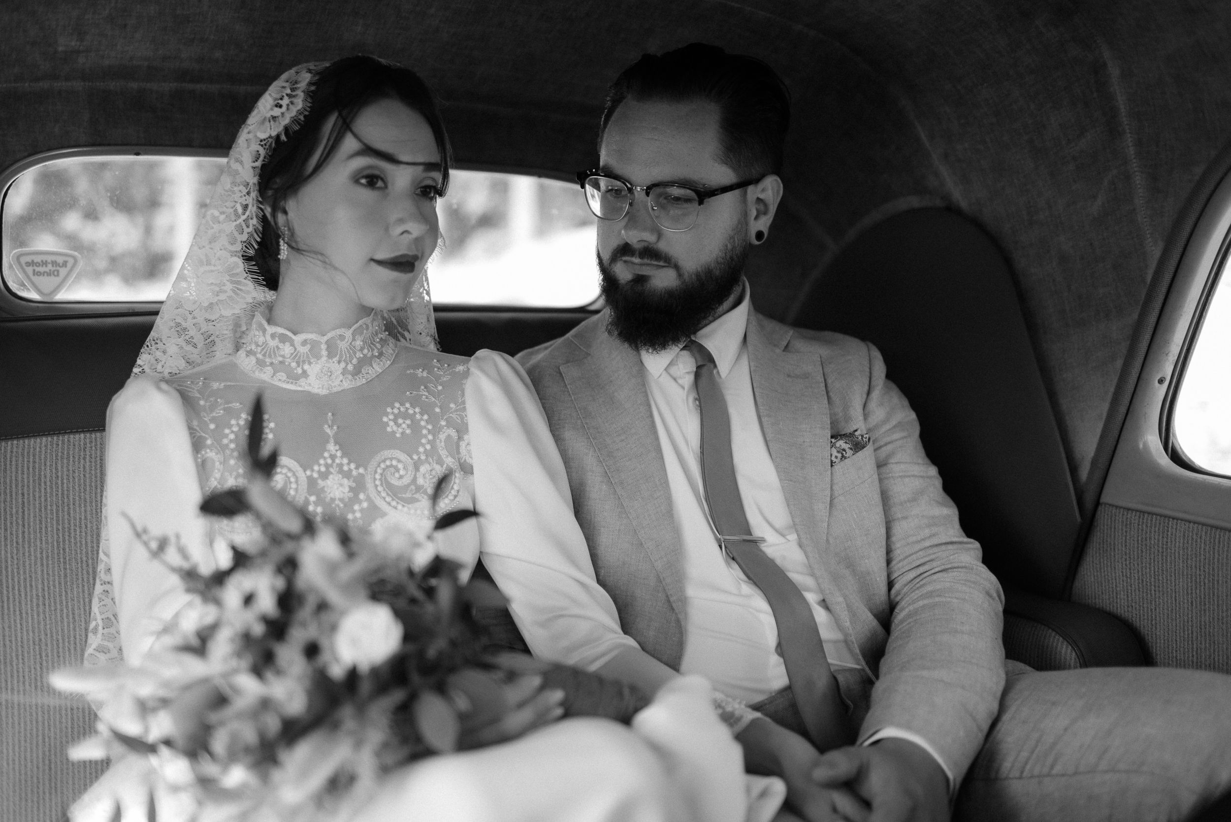 A vintage-style black and white photo of newlyweds sitting in a classic car.