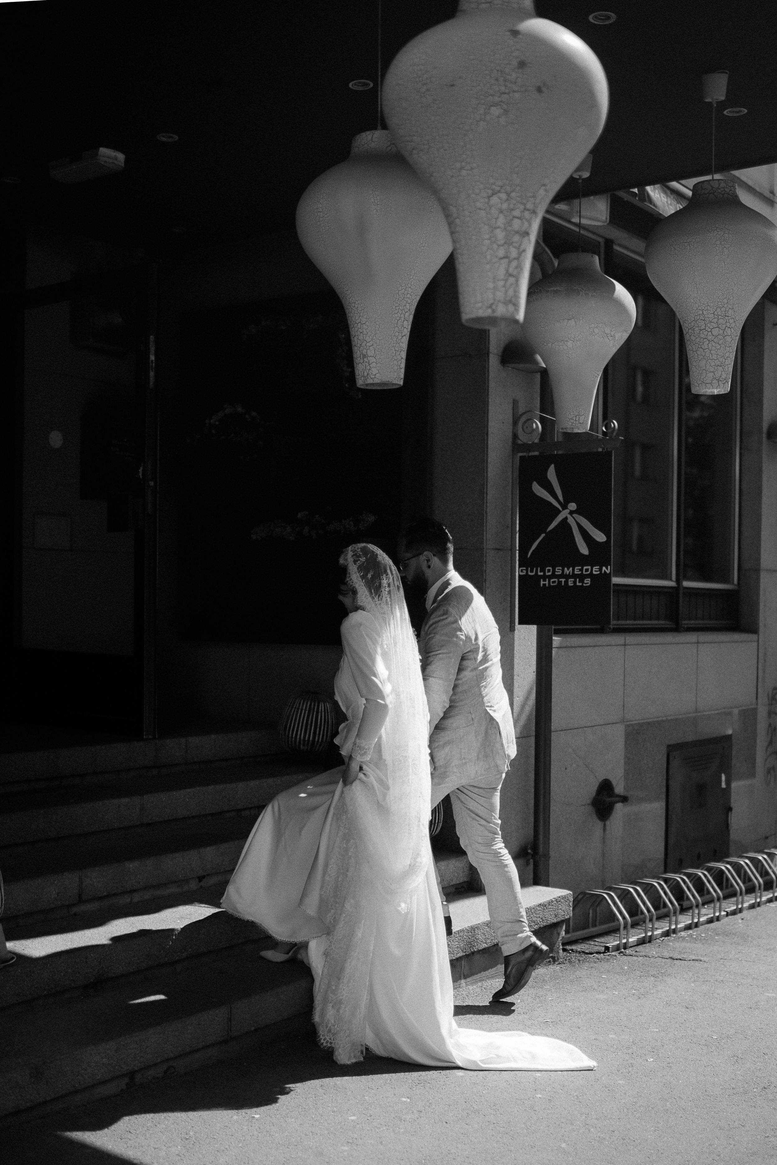 A dramatic black and white photo of newlyweds walking under modern pendant lights.