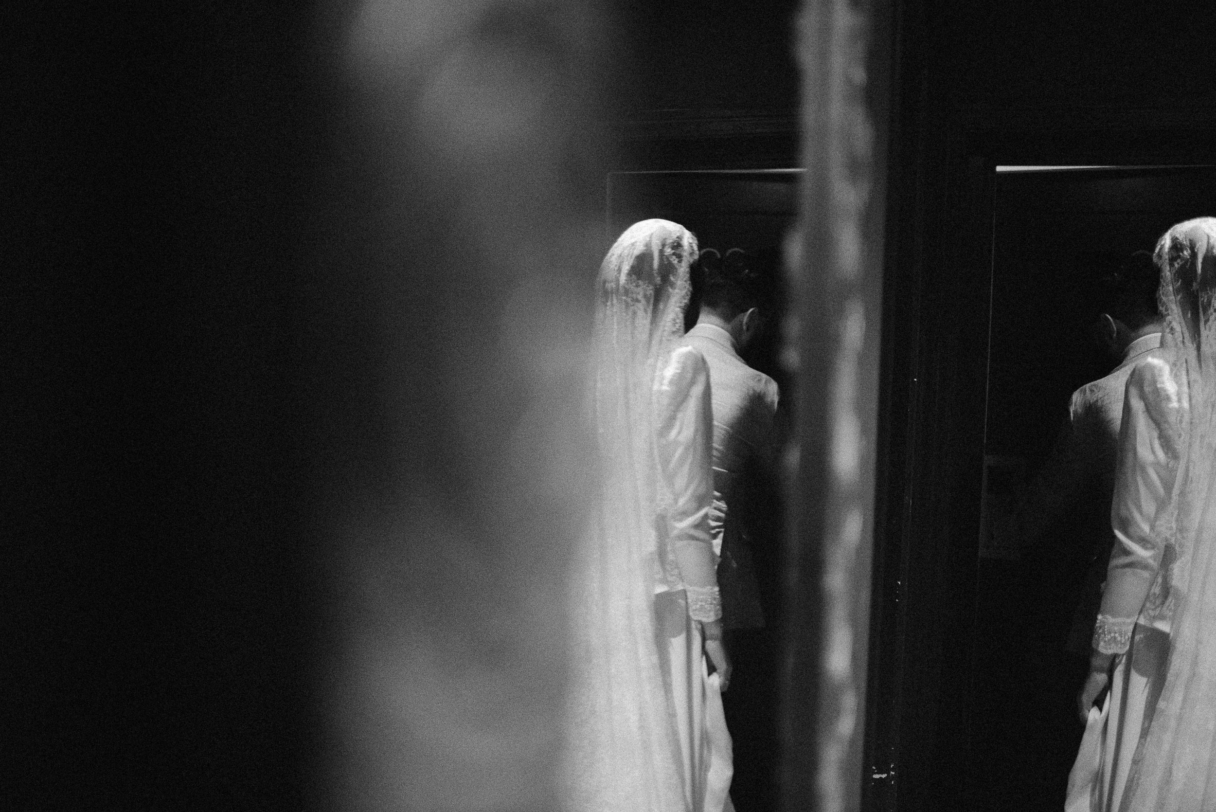 A black and white reflection shot of a bride getting ready in front of a mirror.