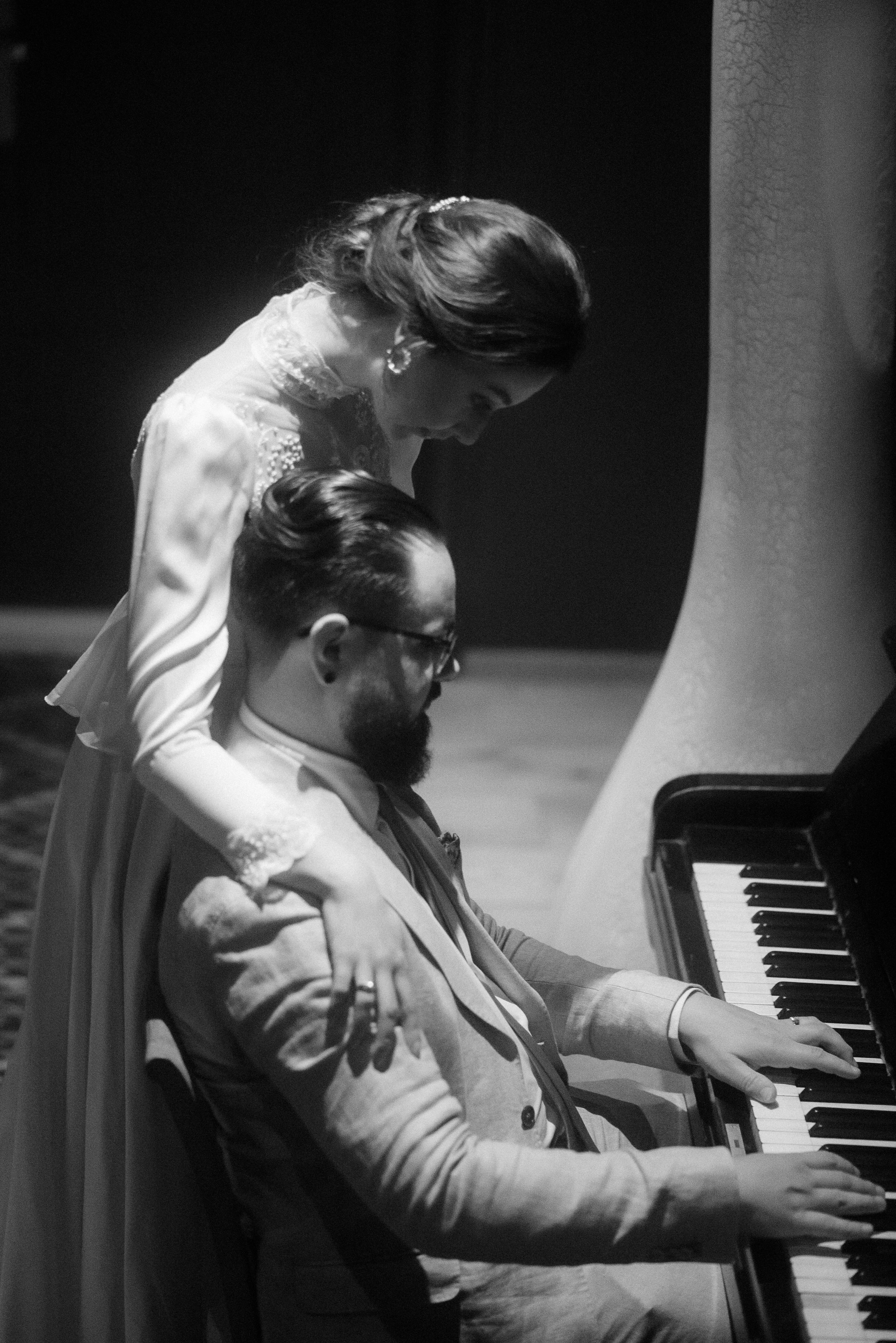 A couple sharing an intimate moment at a piano in elegant vintage attire.