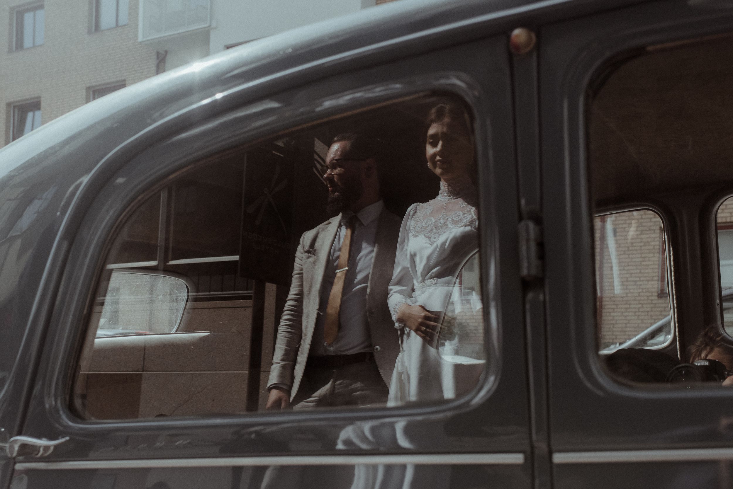 A couple sitting in a classic vintage car looking through the window.