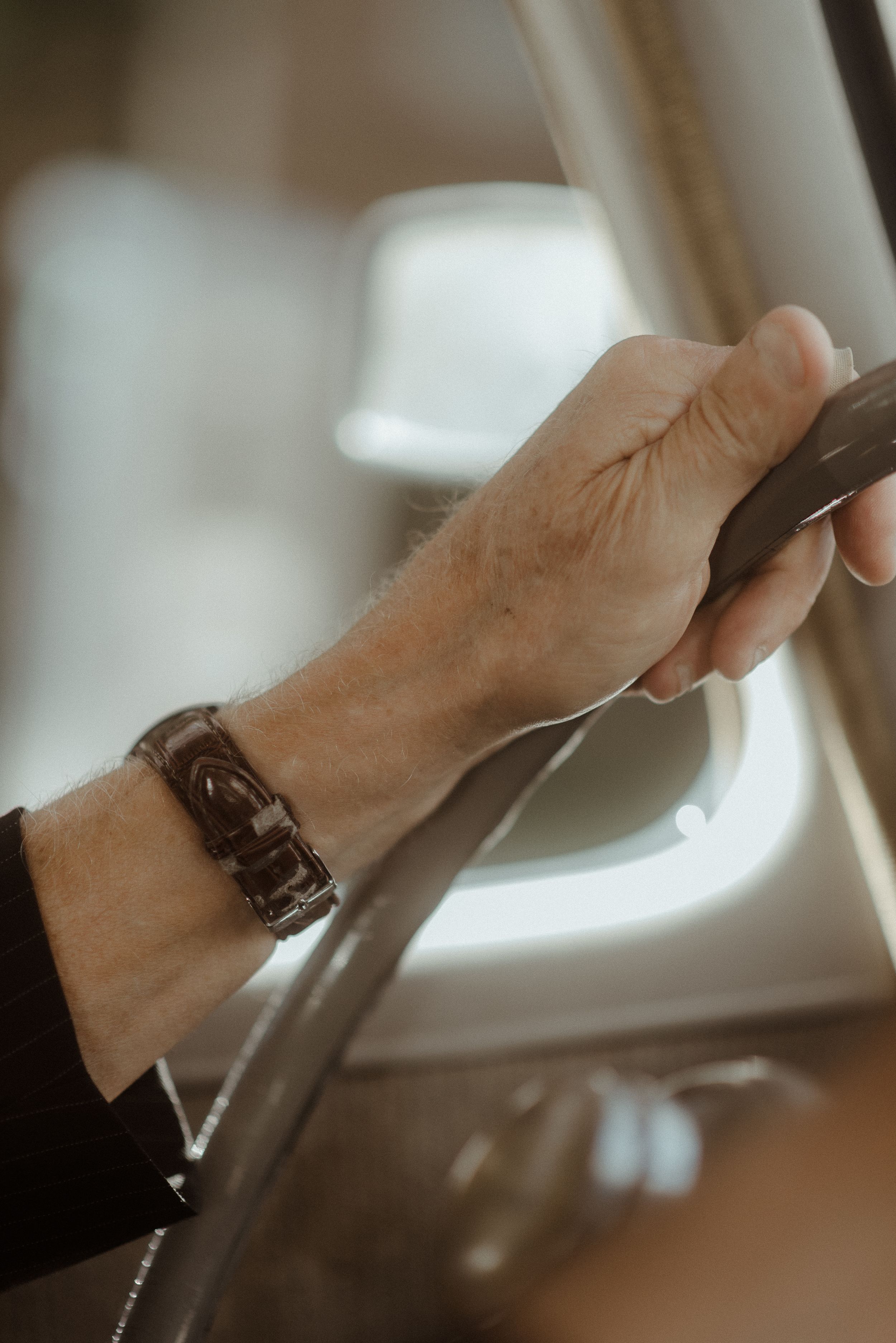Close up of a hand wearing a leather bracelet gripping a steering wheel.