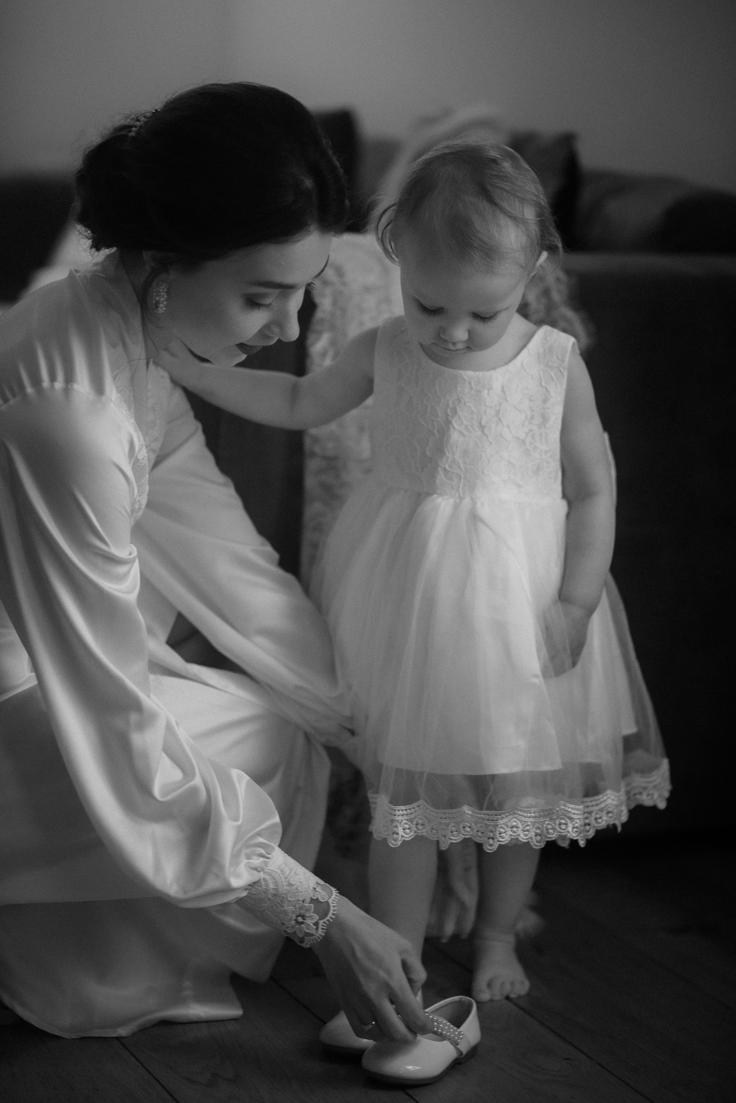 Tender moment of helping a small child in a white lace dress with shoes.