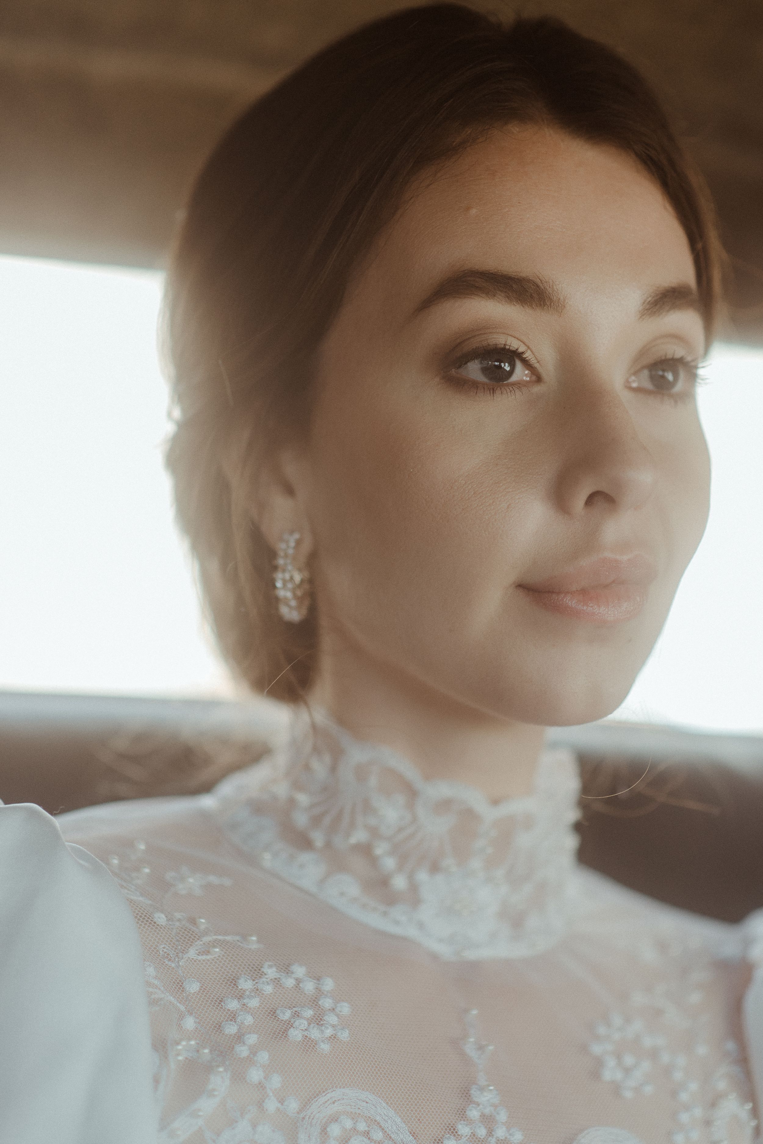 Close-up portrait of a bride wearing an elegant high-neck lace wedding dress with delicate earrings.
