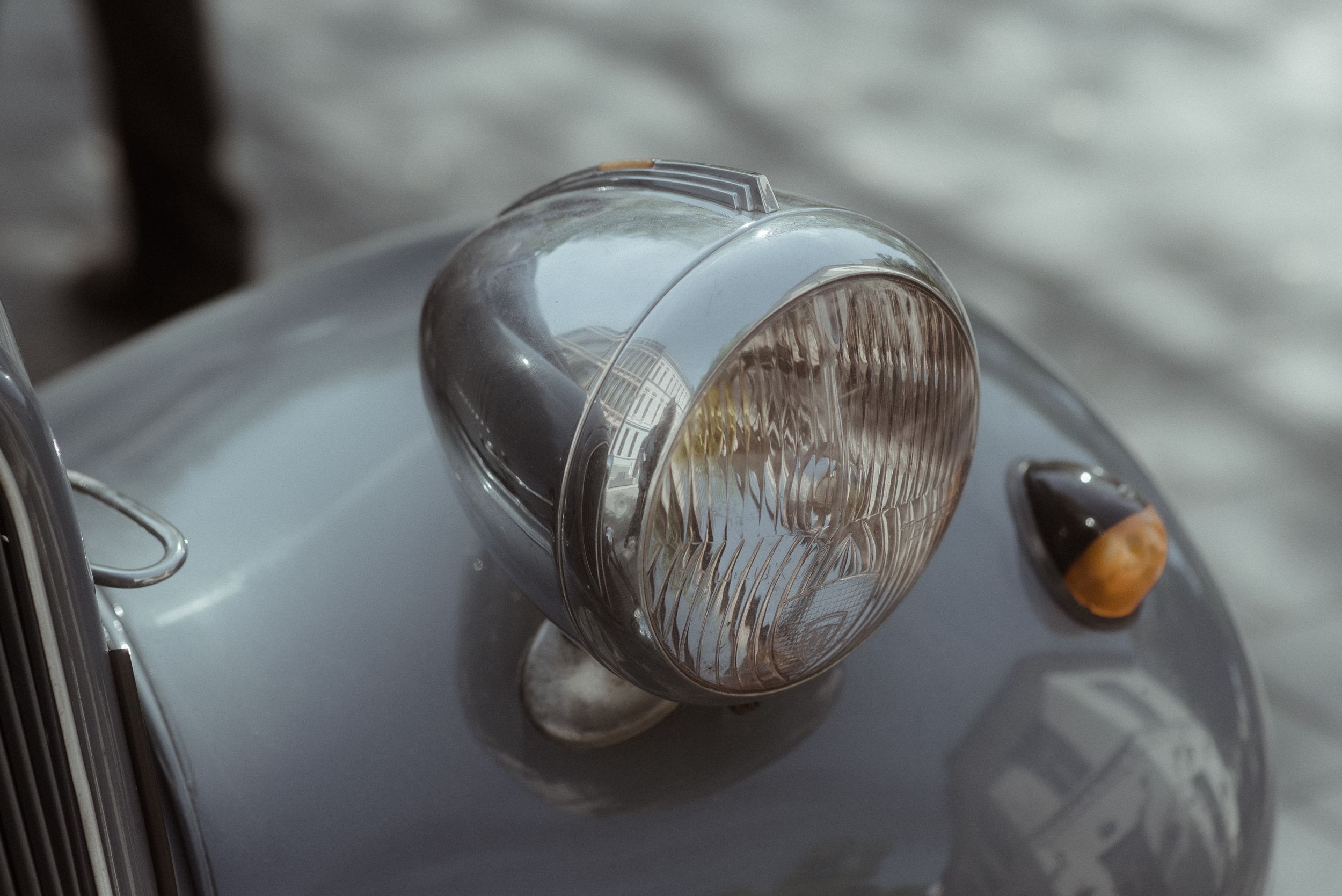Vintage headlight detail of a classic car in soft silver tones.