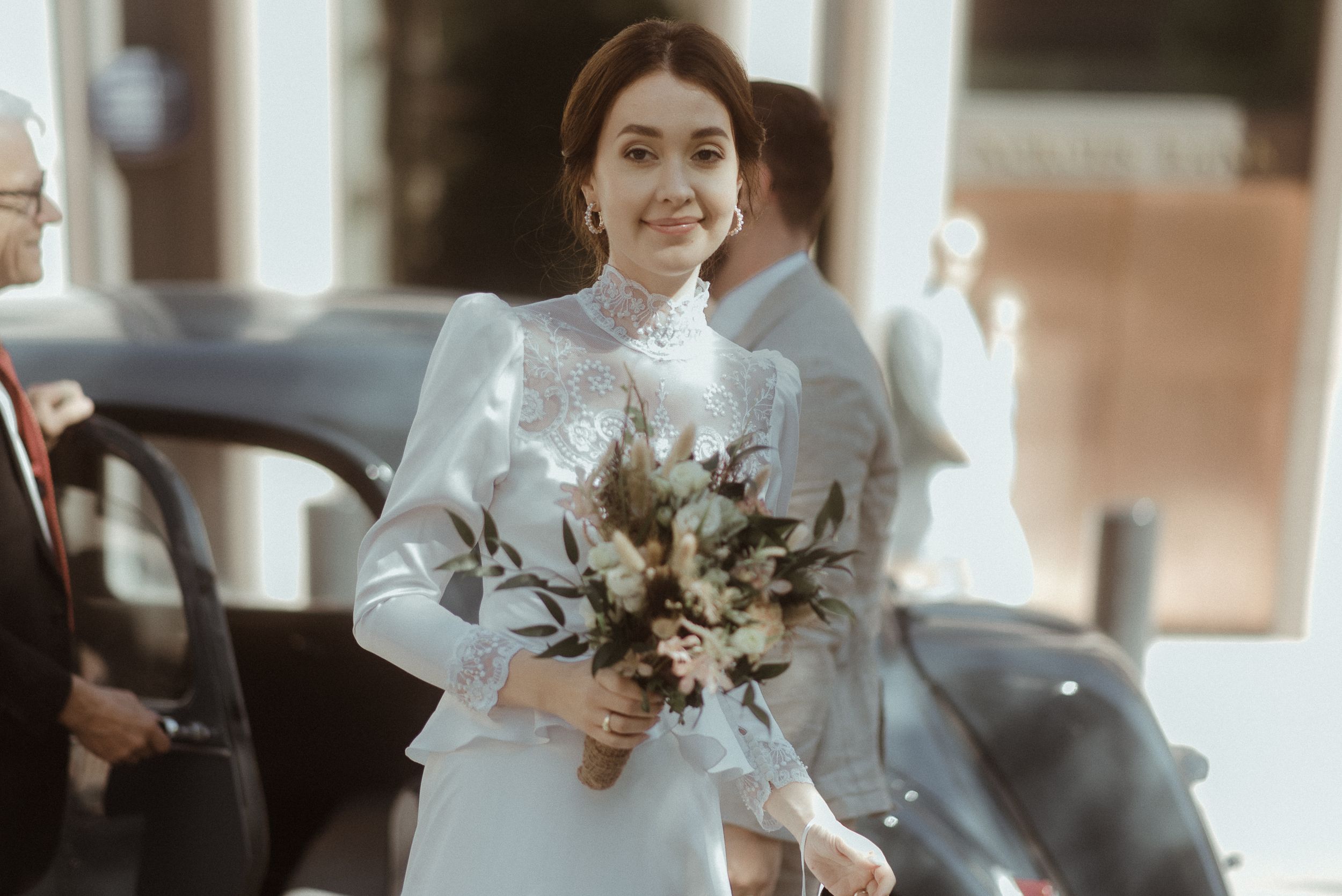 Bride in white high-neck dress holding a neutral-toned bouquet during her wedding day.
