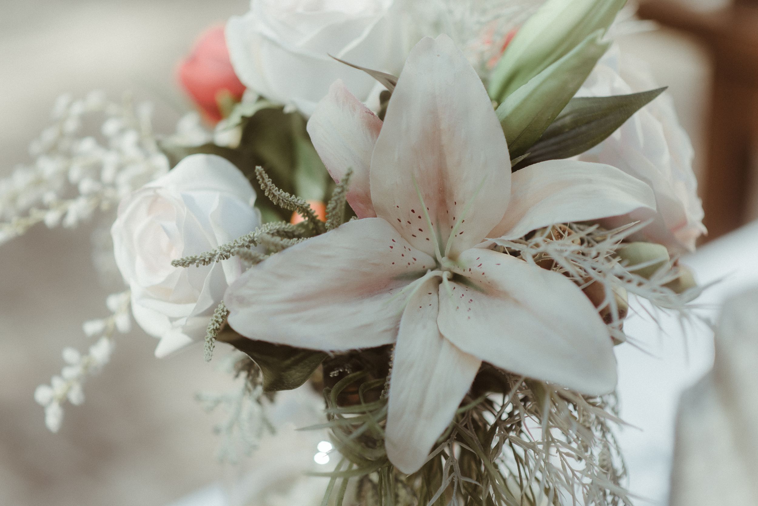 A delicate white lily and rose wedding bouquet with soft pink accents.