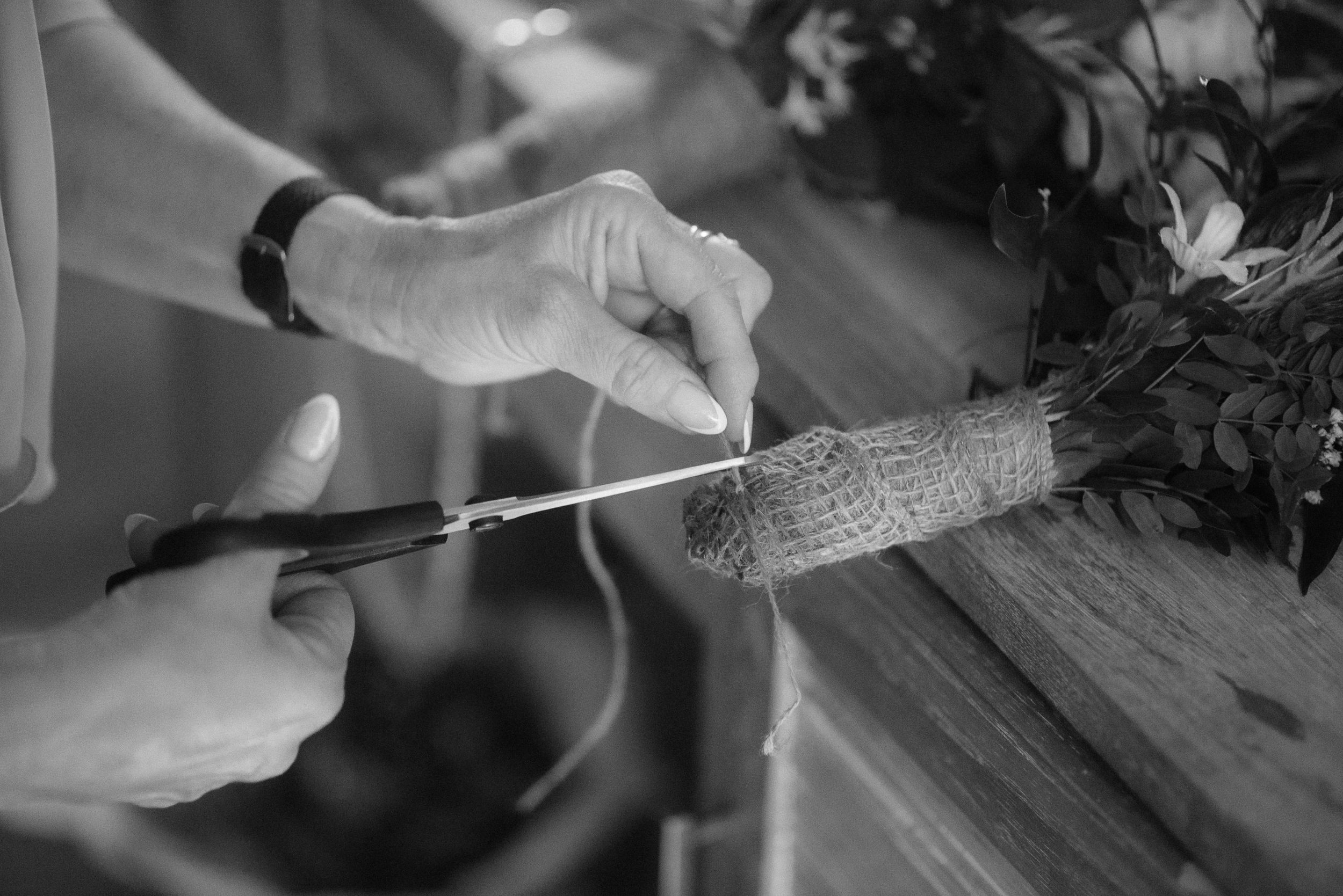 Hands carefully cutting paper with scissors next to floral arrangement.