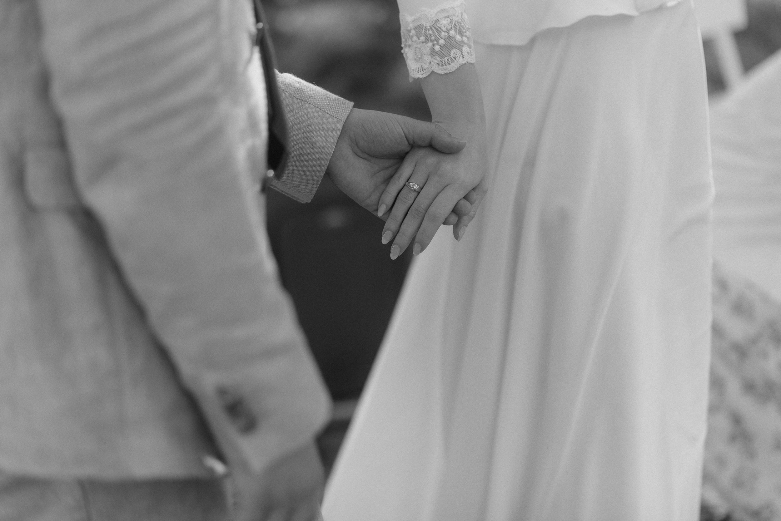 A close-up black and white shot of hands wearing wedding rings.