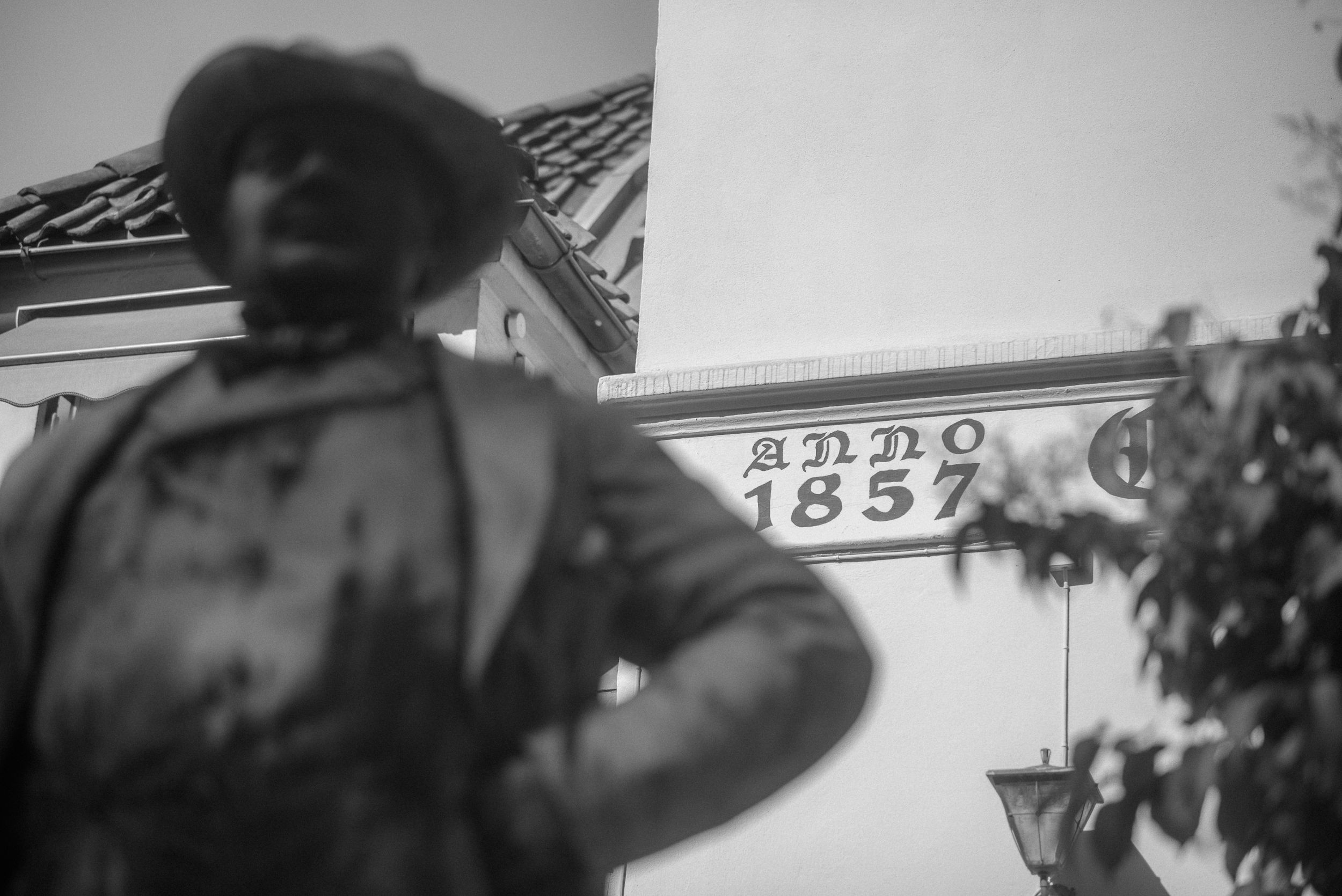 A blurred vintage photograph showing a figure standing near text that reads 1857.