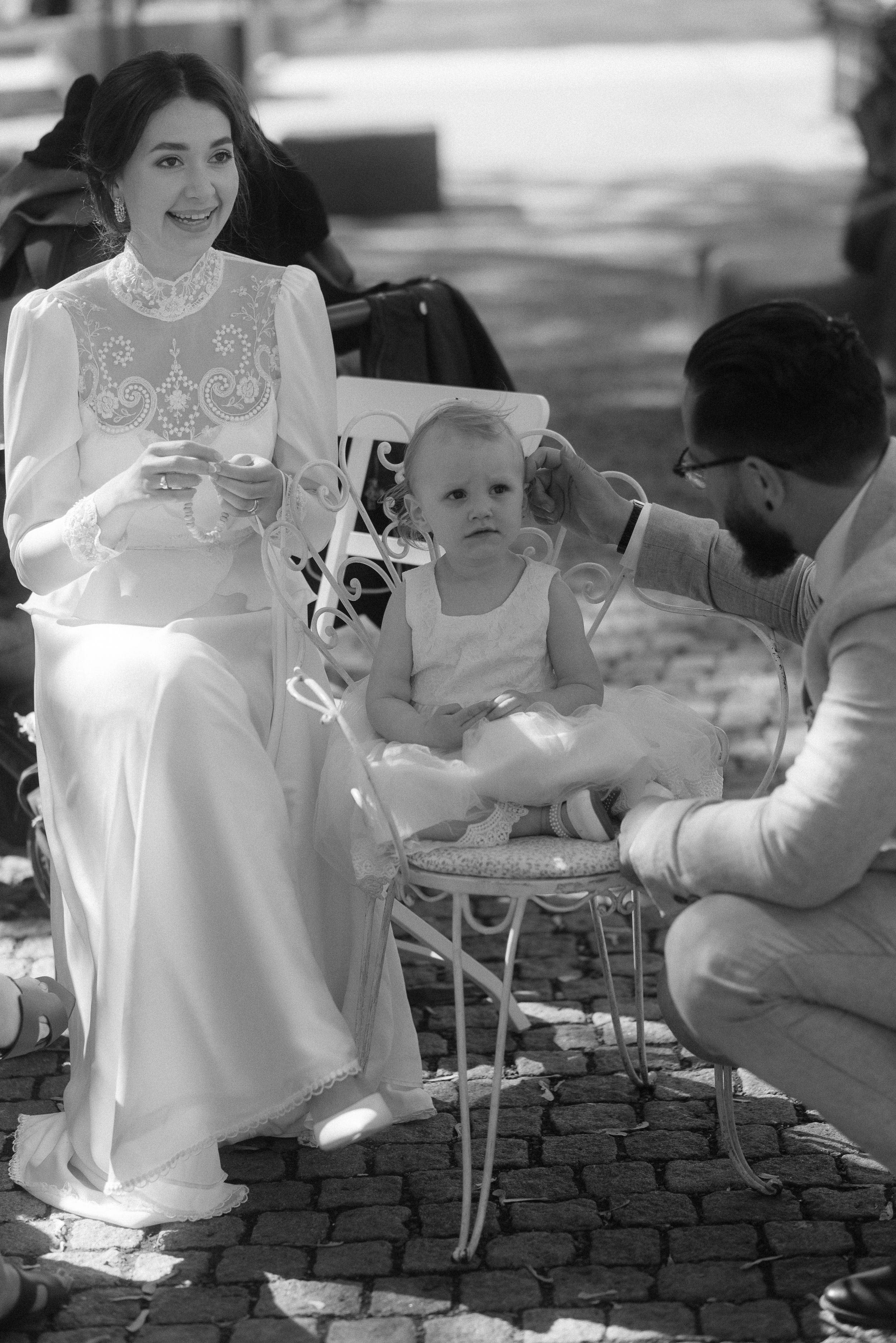 Family enjoying a moment together on cobblestone pavement with a baby in white dress.