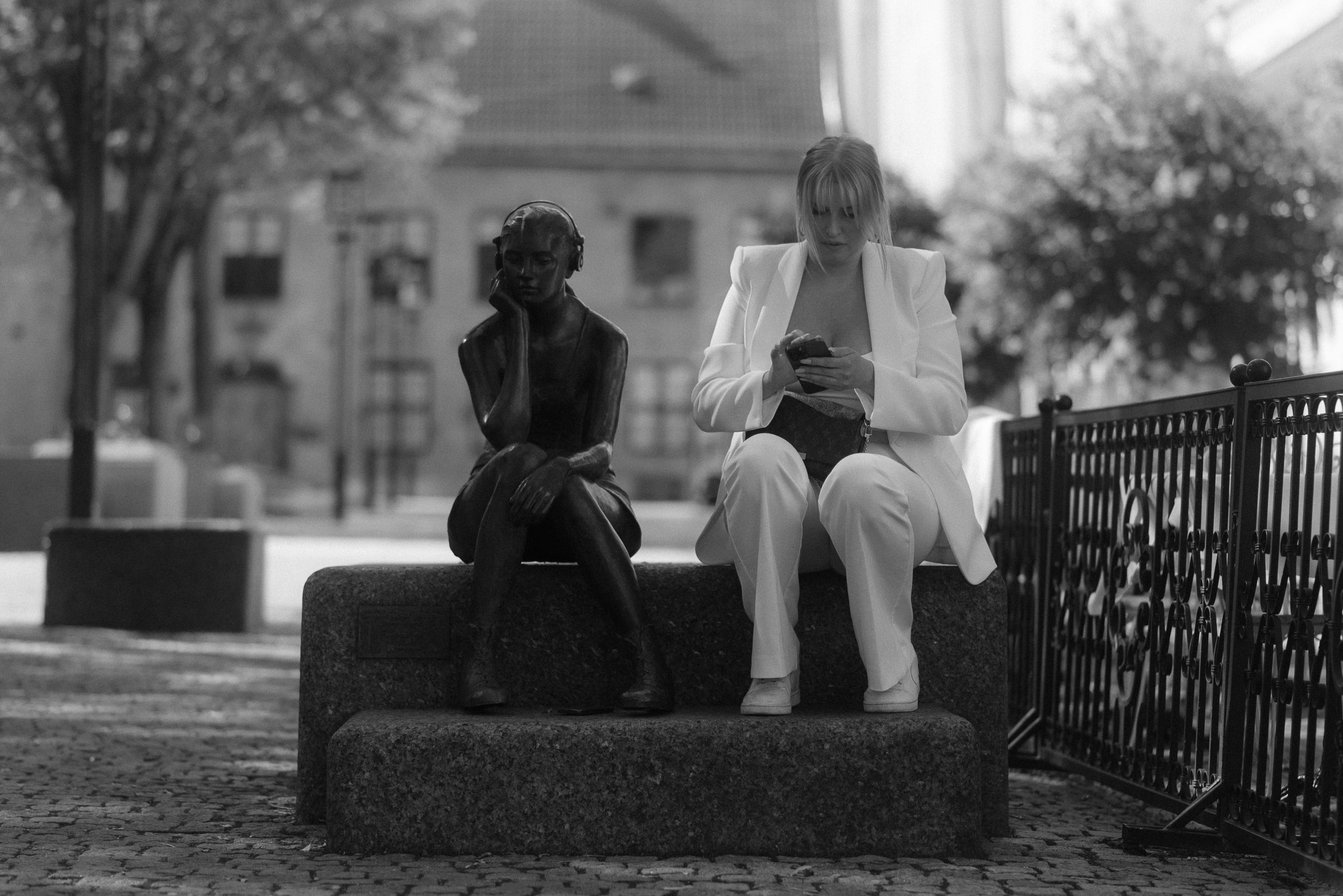 Two children sit on a stone wall near an iron fence in a black and white photograph.