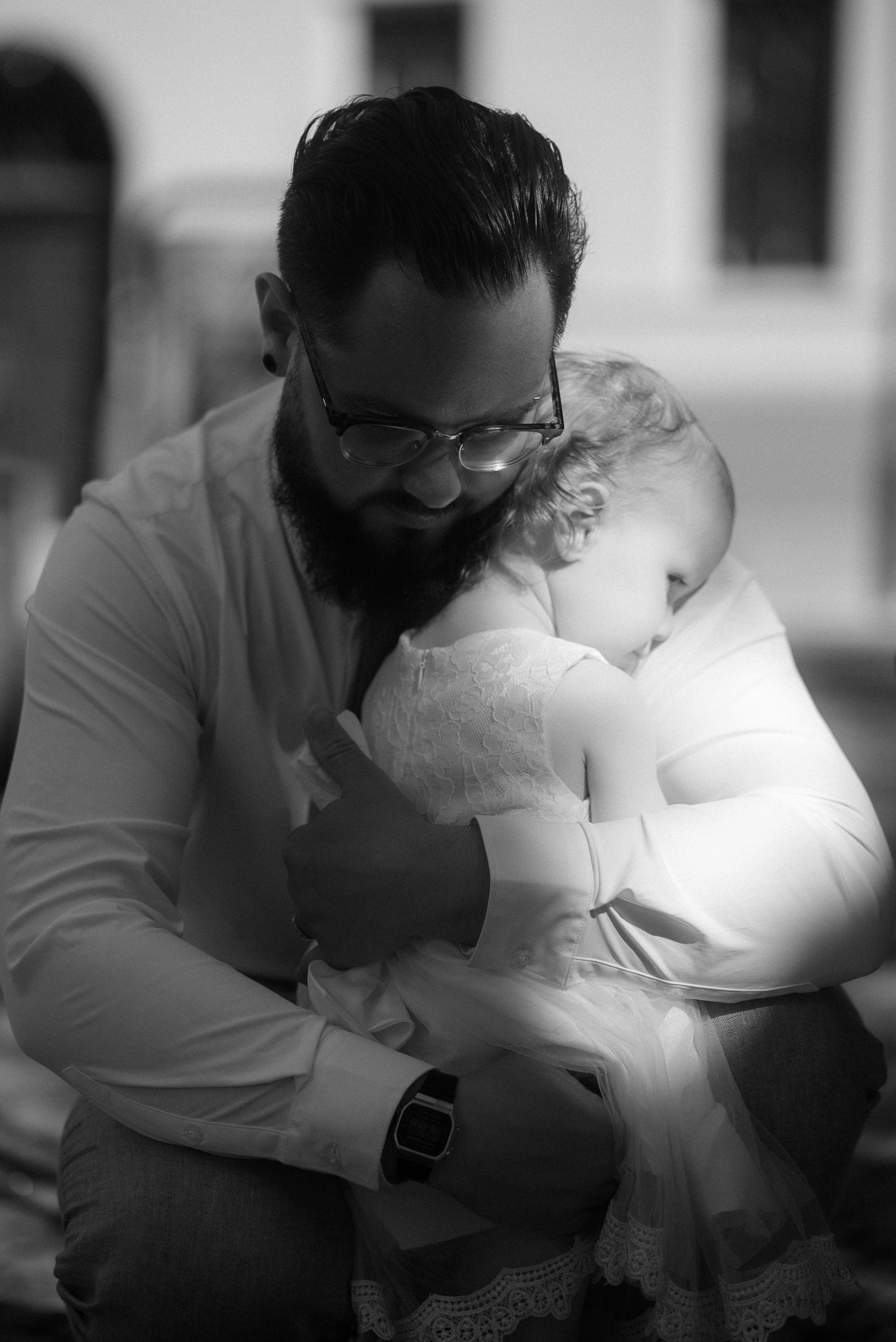 An intimate black and white portrait of a parent holding a baby in white clothing.