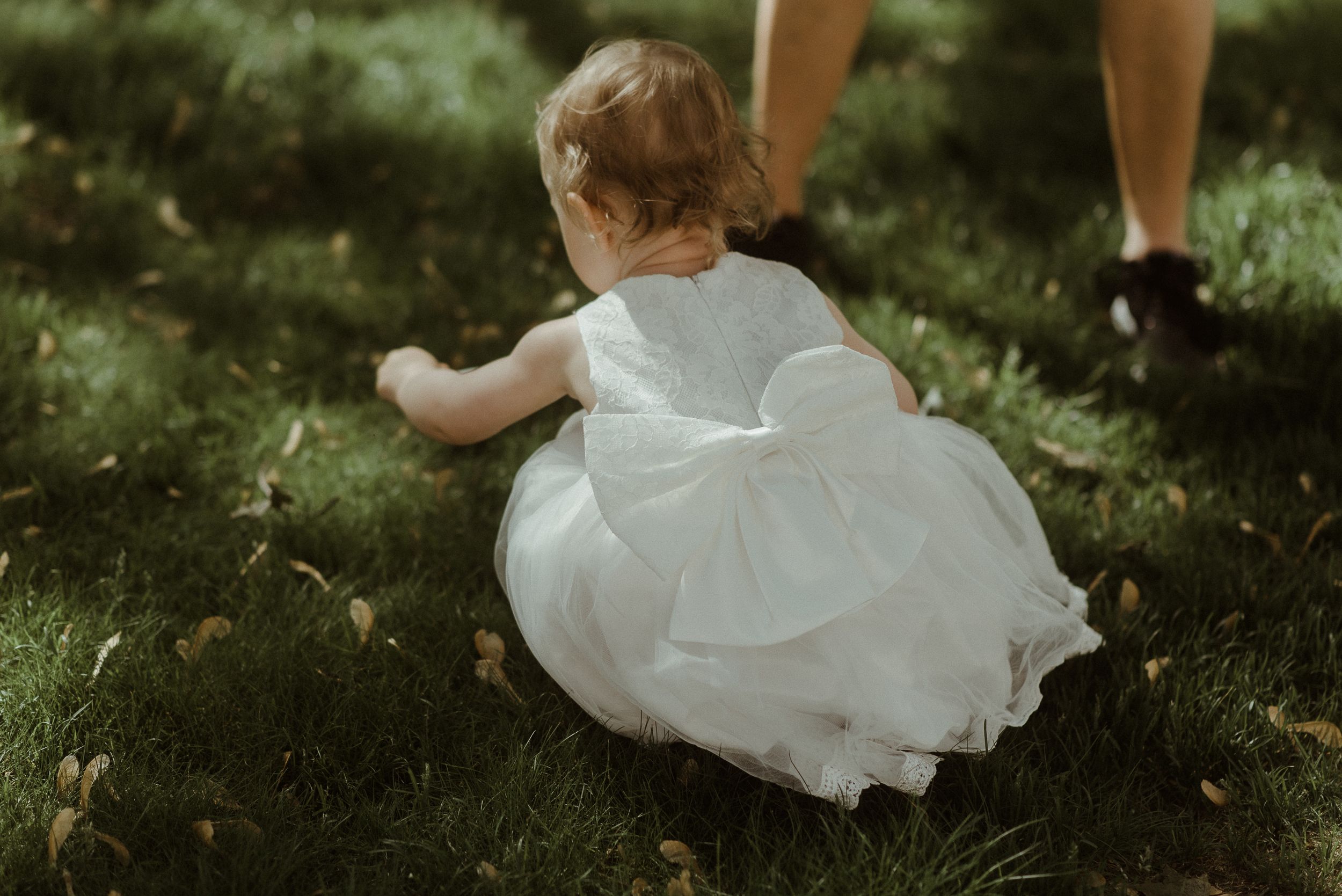A small figure in a white dress crawling on grass in dappled sunlight.