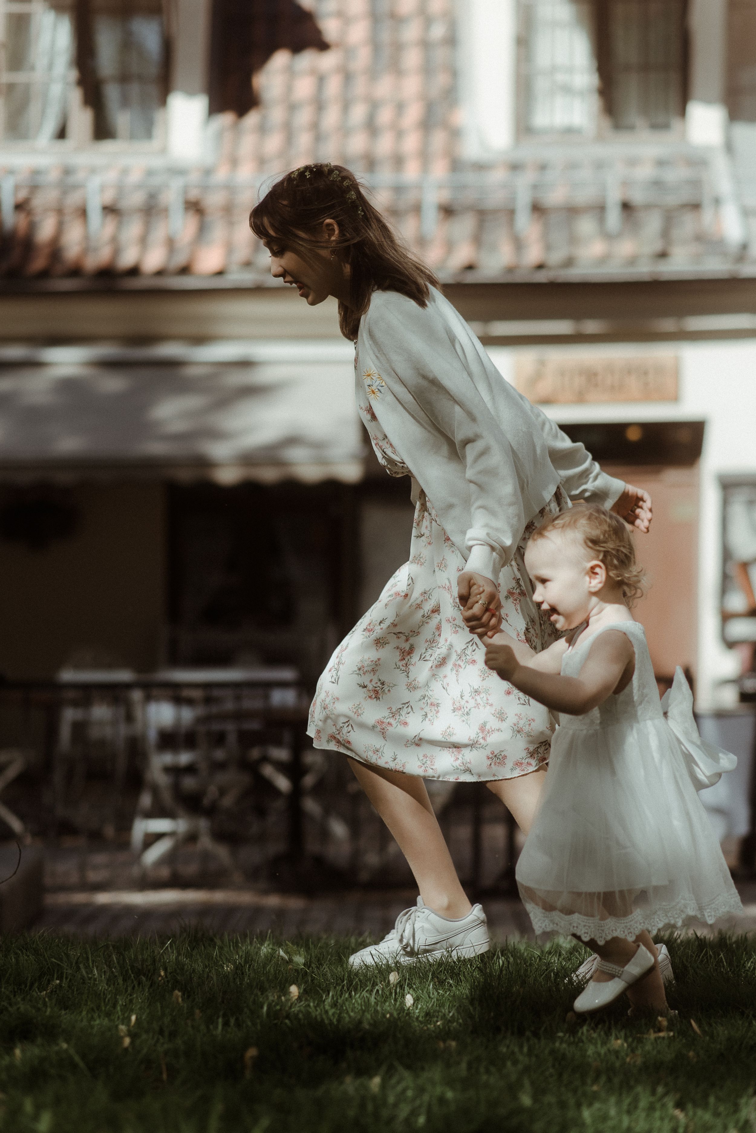 Two figures in white dresses dancing together on a grassy area near a building.