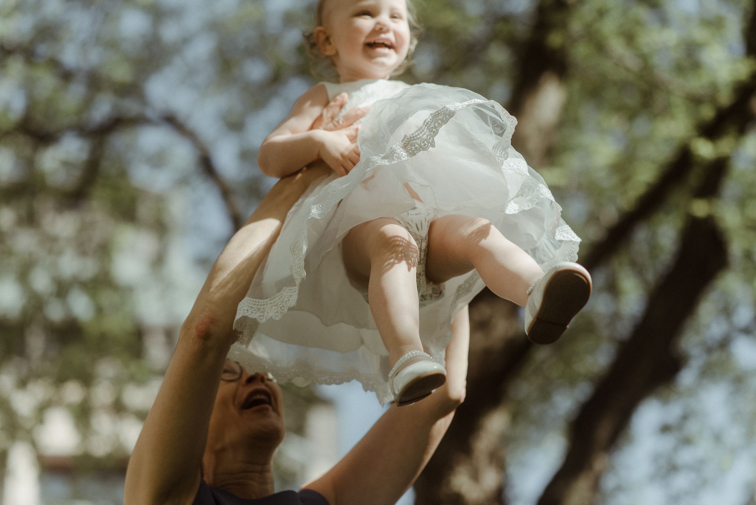 A figure in a white dress is lifted up against a backdrop of trees and sky.
