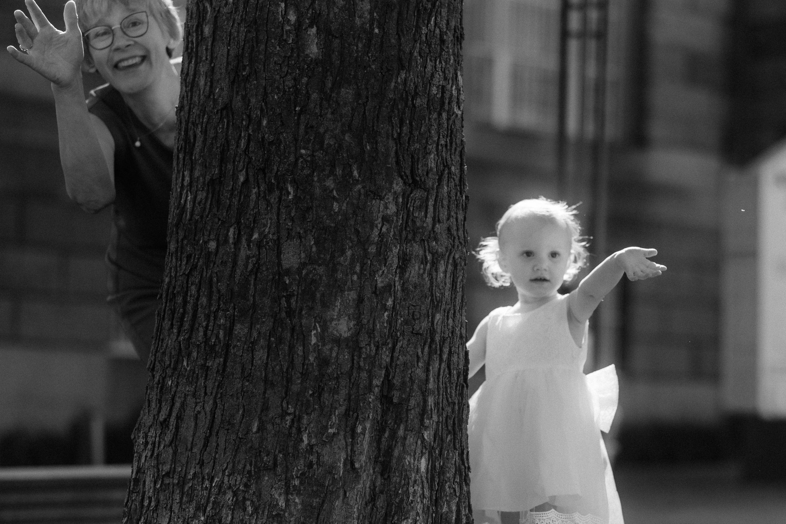 A playful scene near a large tree trunk captured in black and white.