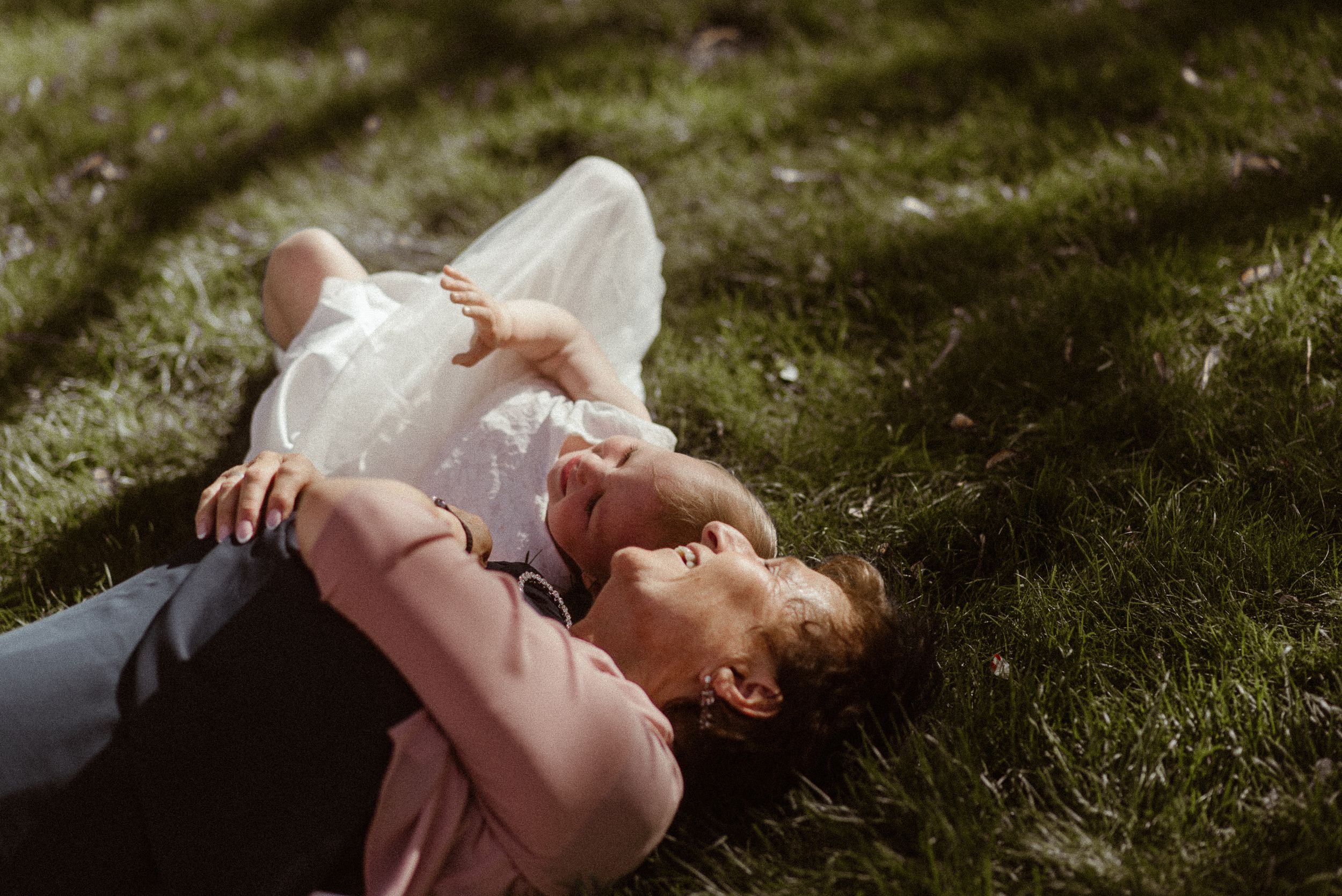 Someone in white clothing lies on green grass during a sunny afternoon.
