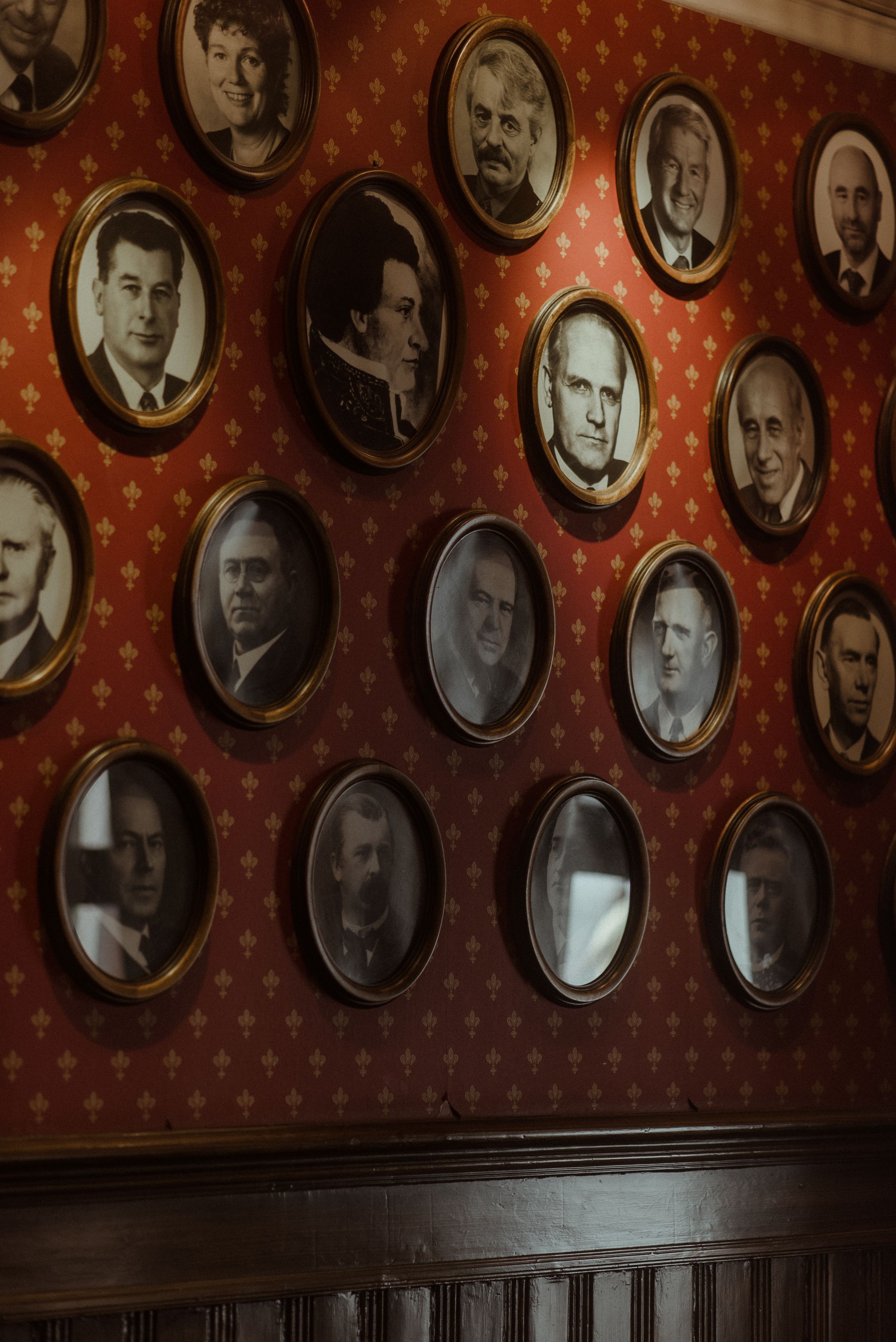 Historical portrait photographs arranged in oval frames on red wallpapered wall.