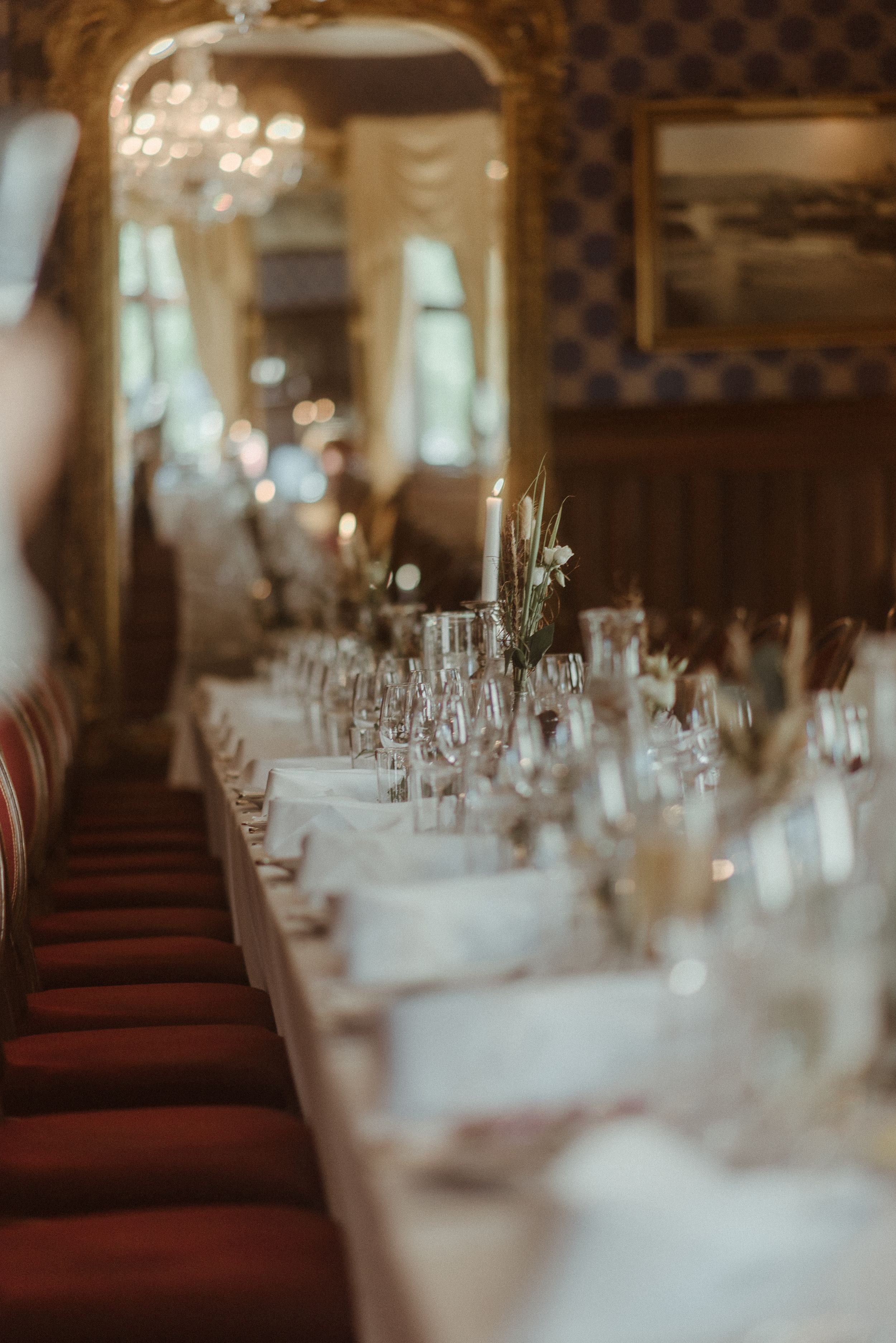 Elegant dining table set for a formal event with red chairs and crystal chandelier in an ornate room.