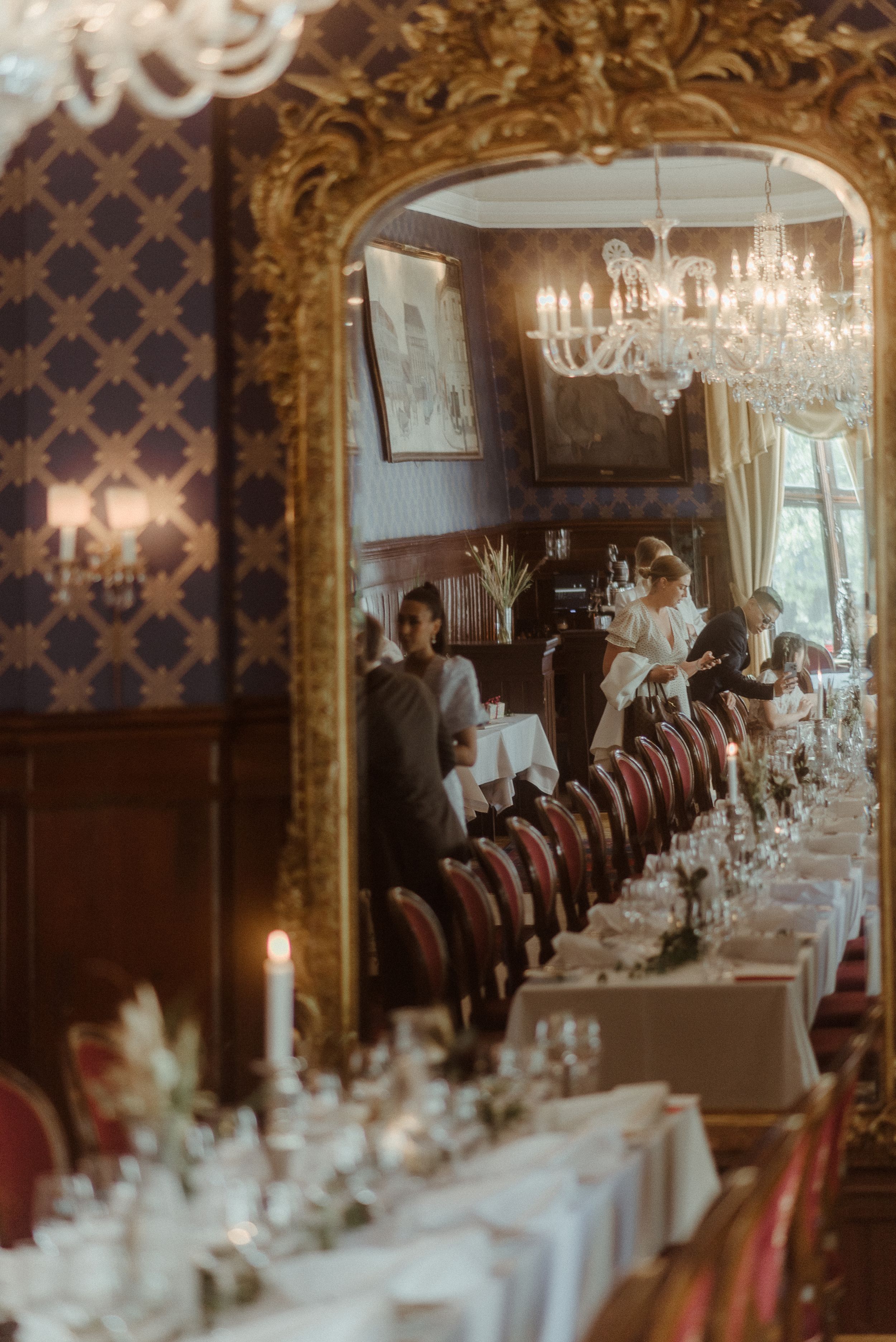 Formal dining room with ornate gold archway, crystal chandeliers, and red velvet chairs set for an event.