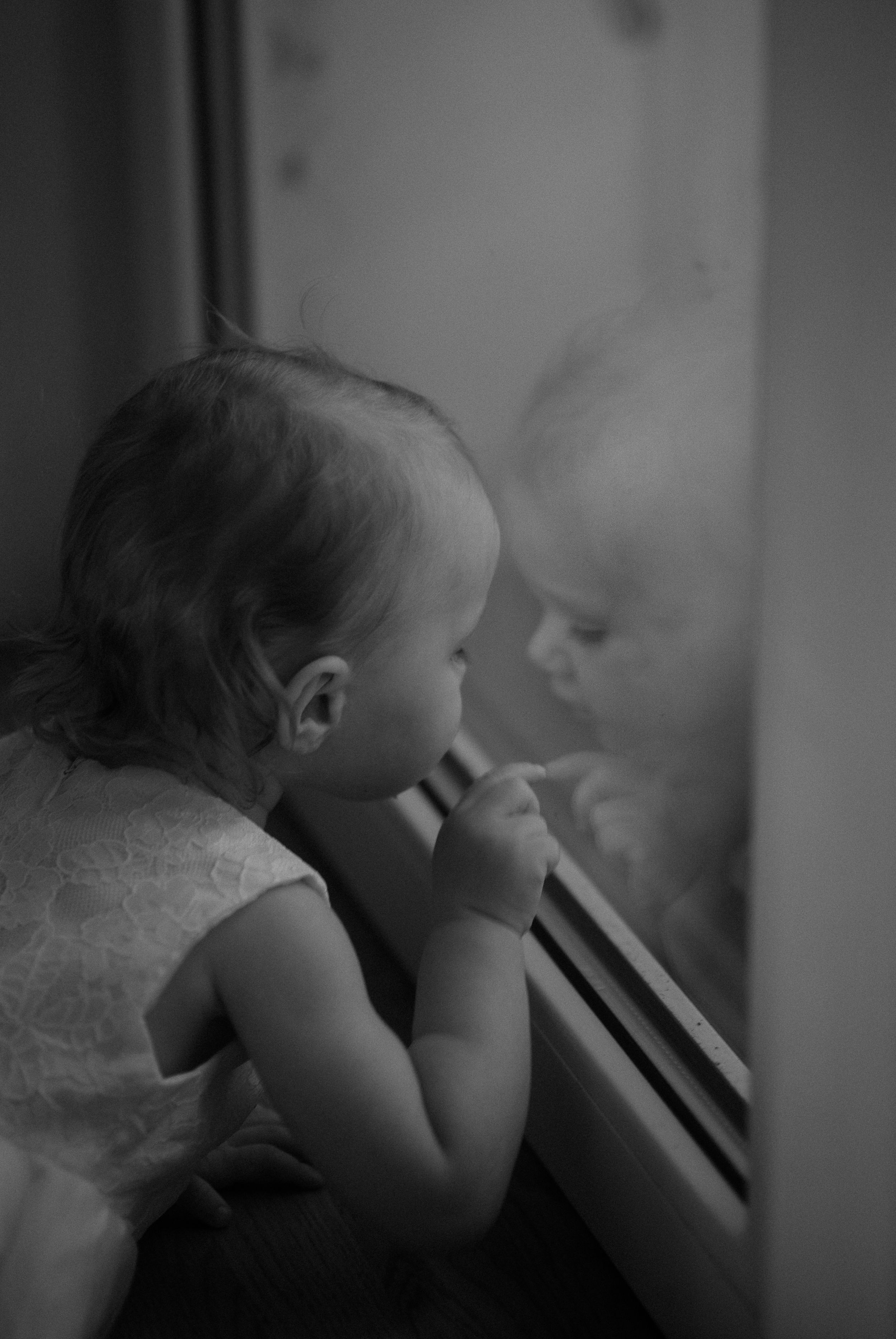 Young child looking through window in dreamy black and white portrait.