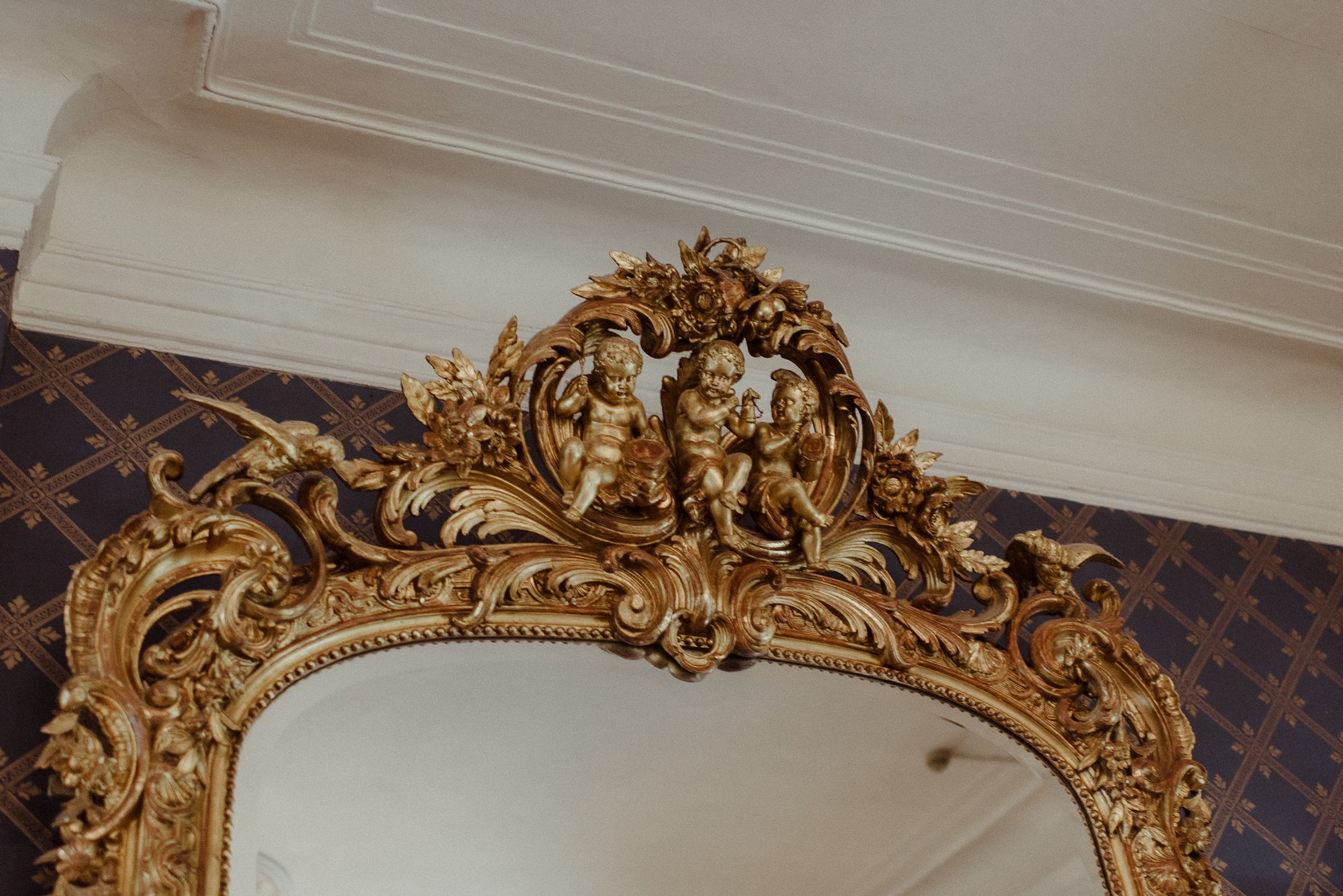 Ornate gold baroque mirror frame detail against blue patterned wallpaper.