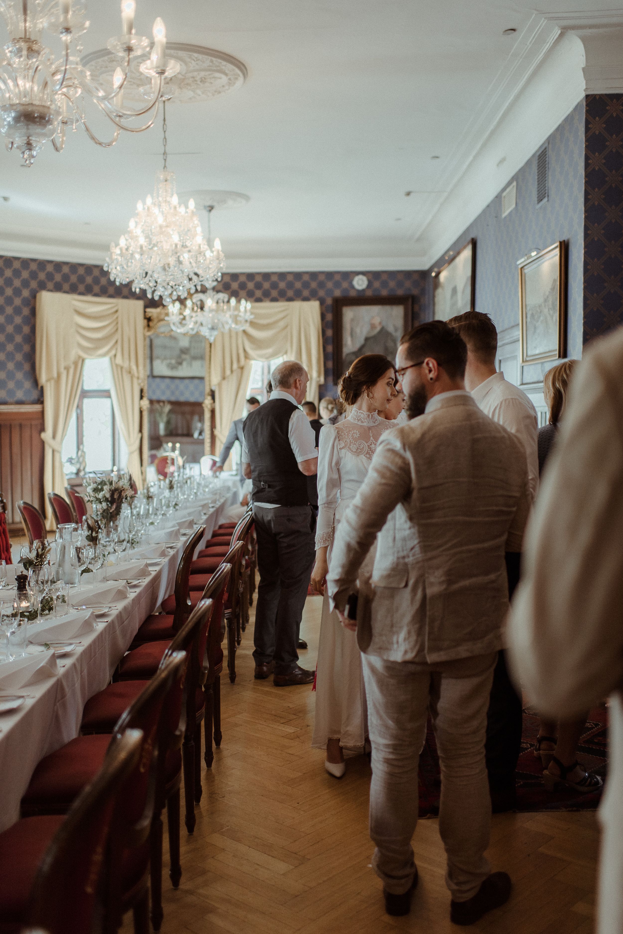 Elegantly decorated dining room with crystal chandeliers and a long white-clothed table set for a formal celebration.