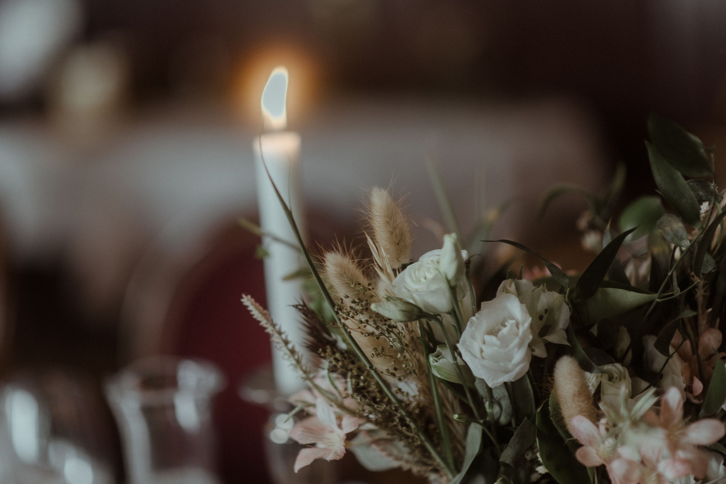 A single lit candle glows softly among delicate floral arrangements.