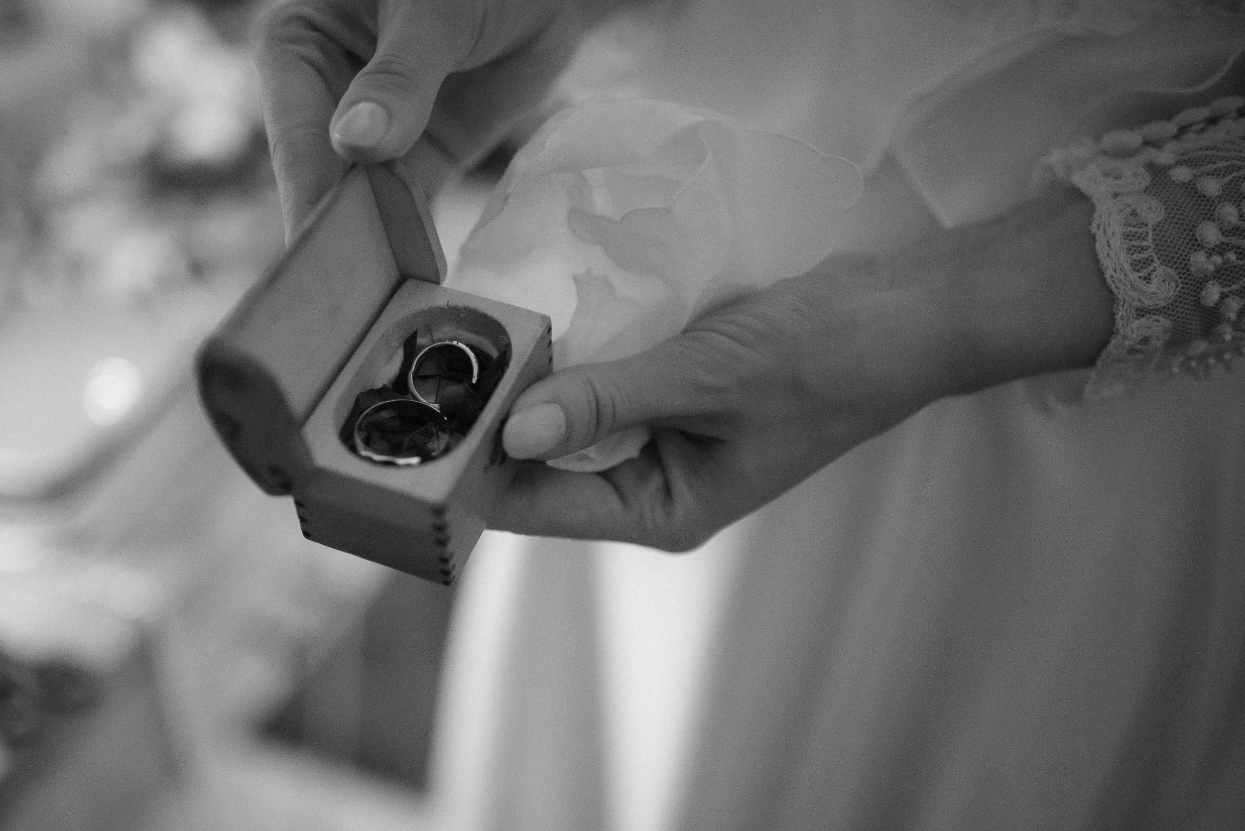 Hands holding small ring box with wedding bands in monochrome photography.