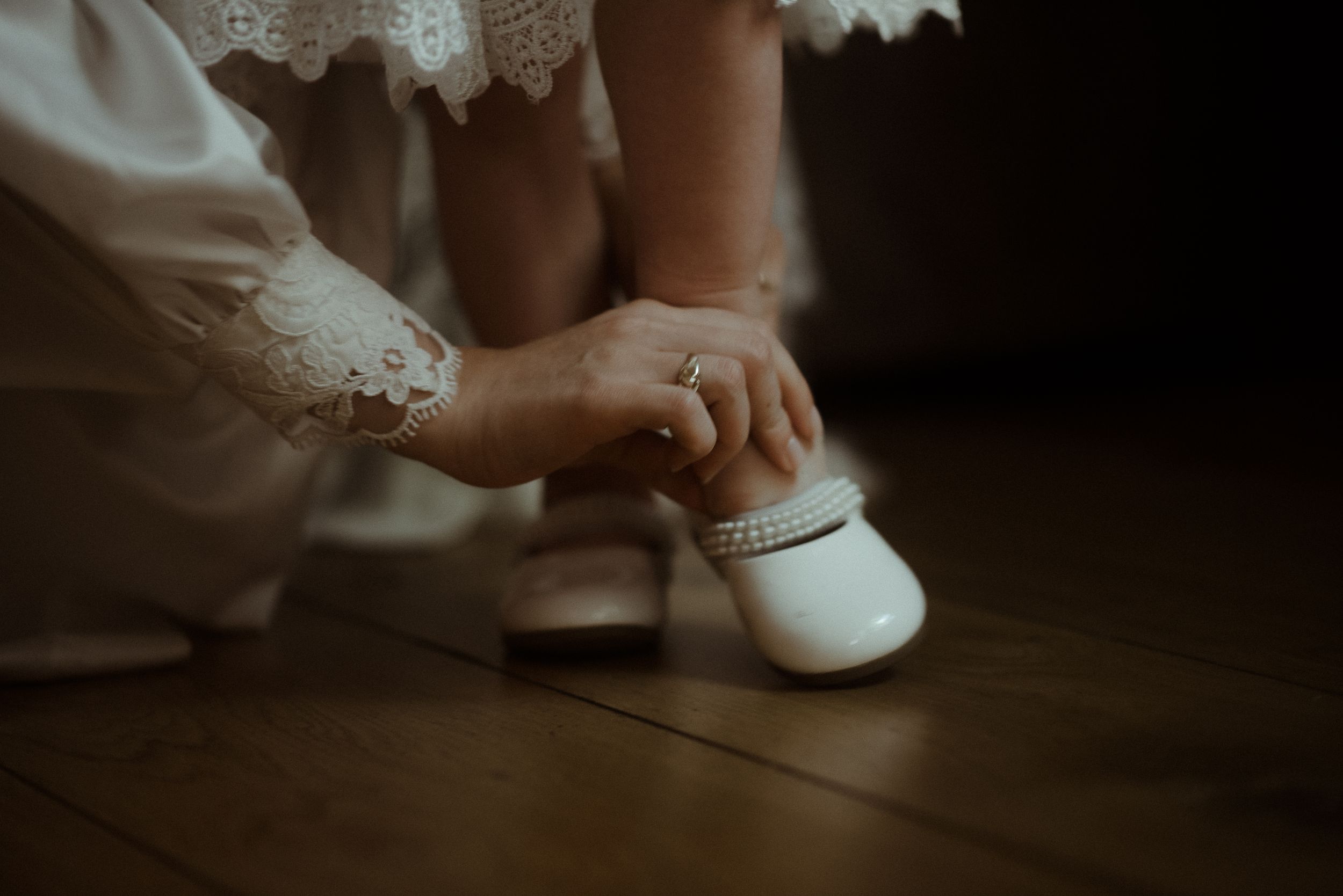 Close-up shot of hands fastening a tiny white shoe on a small foot.