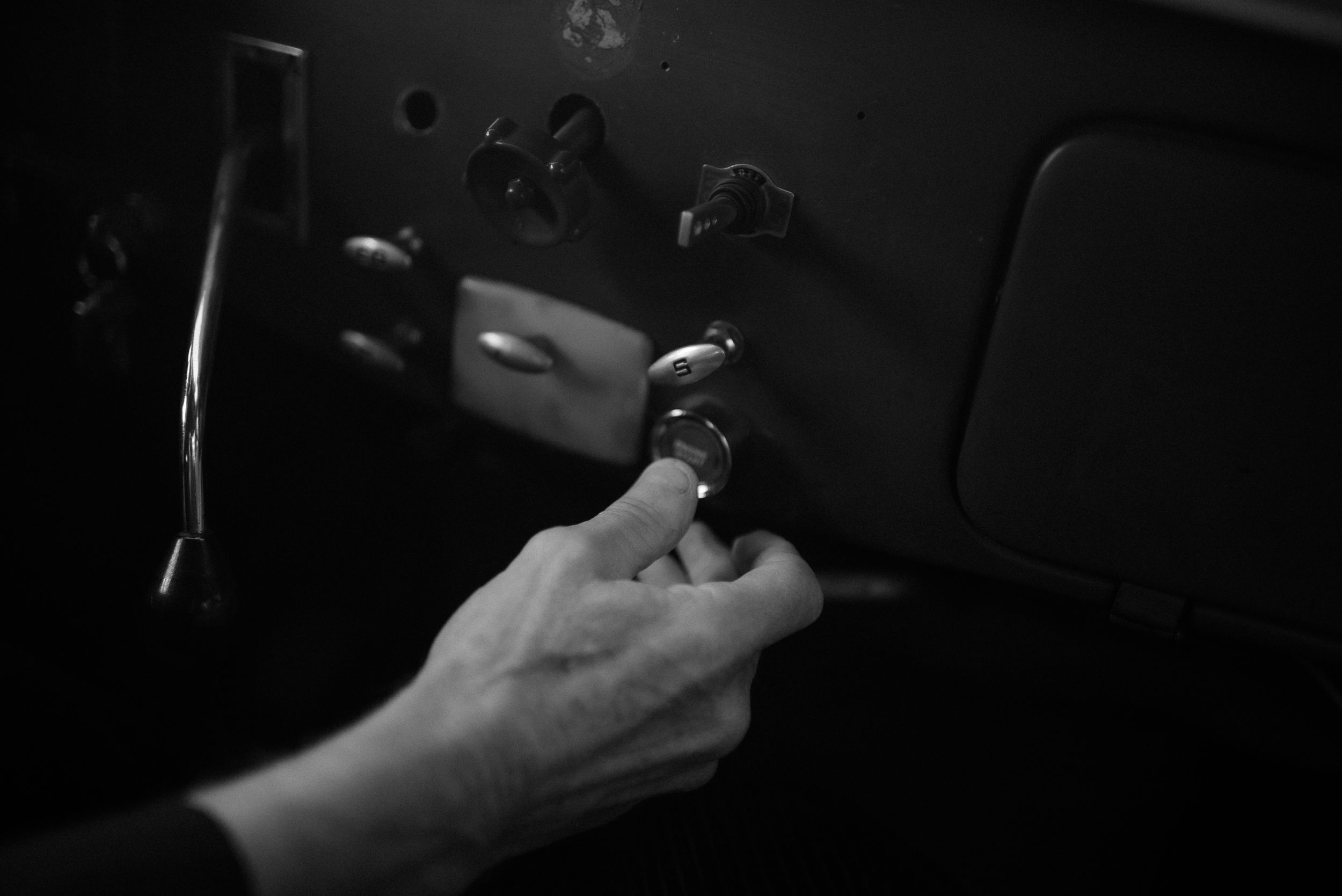 Black and white image of hands holding a steering wheel in a darkened car interior.