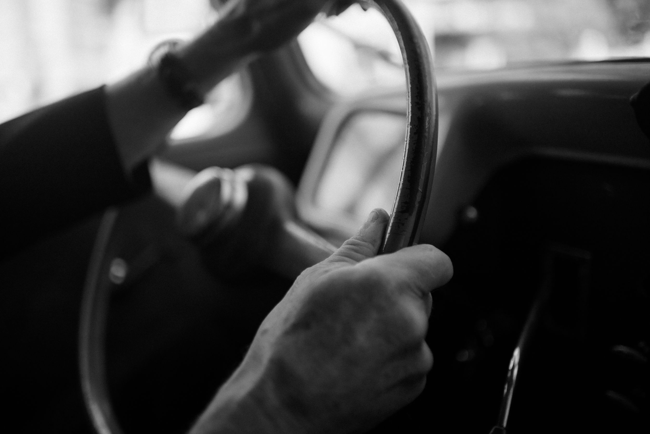 Black and white close-up of hands gripping a vintage car steering wheel.