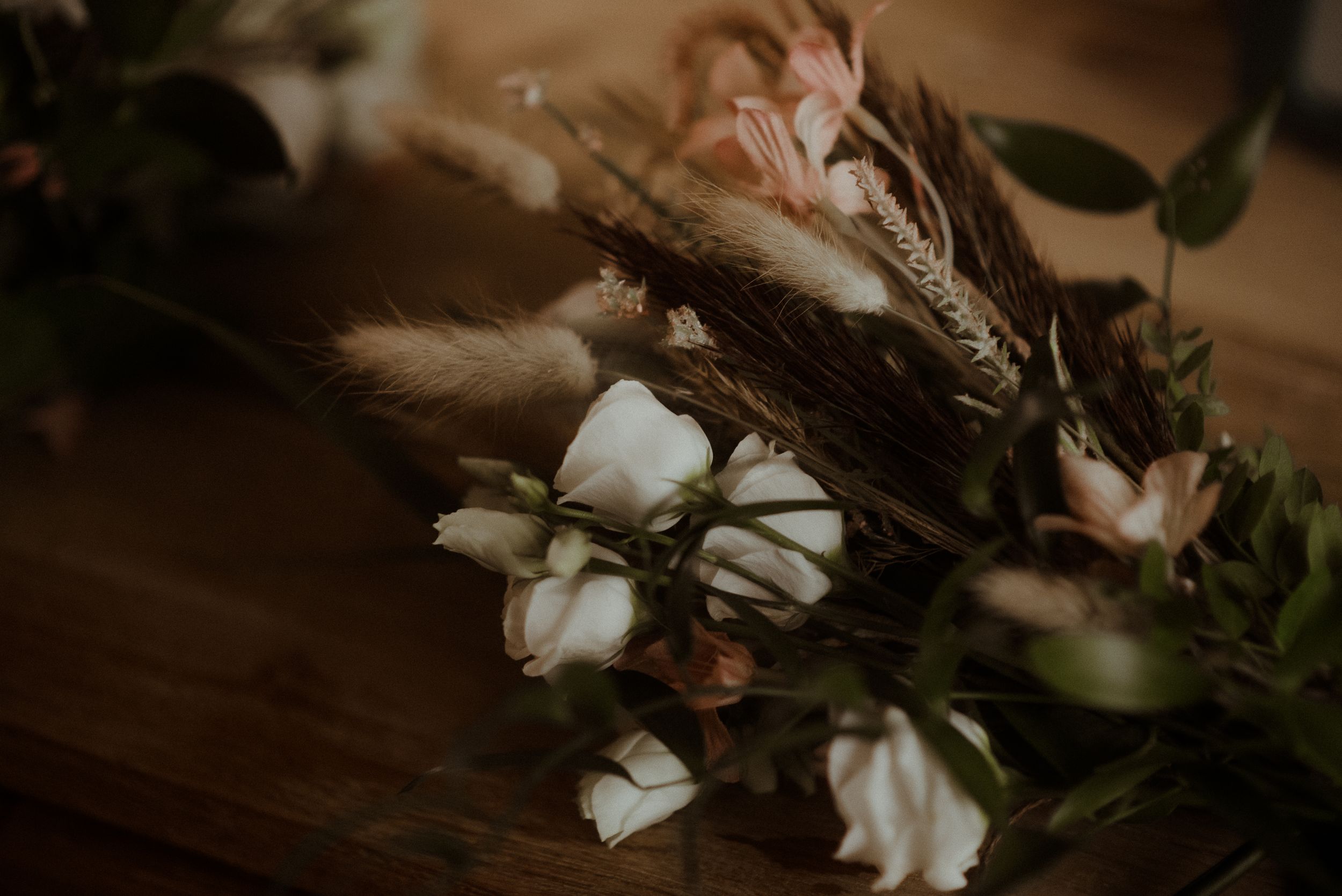 Romantic floral arrangement with white roses and dried flowers in moody lighting.
