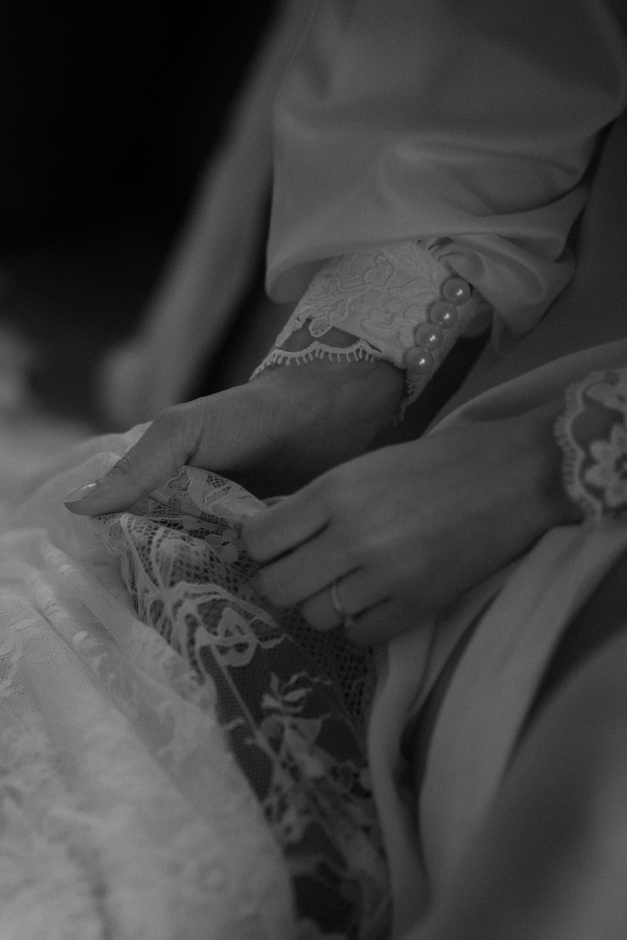 Detail shot of hands resting on intricate lace fabric in black and white.