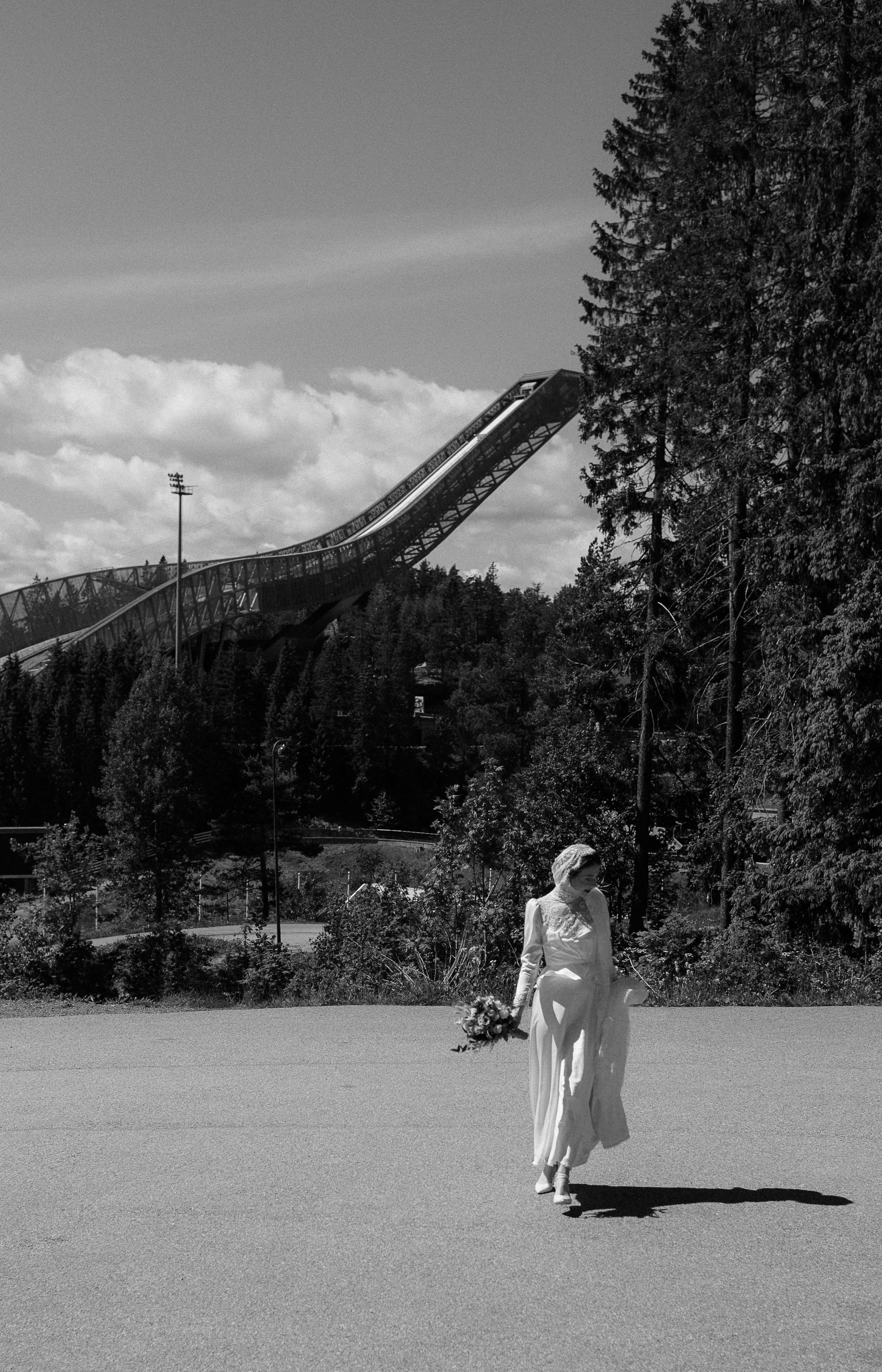 A dramatic ski jump tower rises above the forest landscape in black and white.