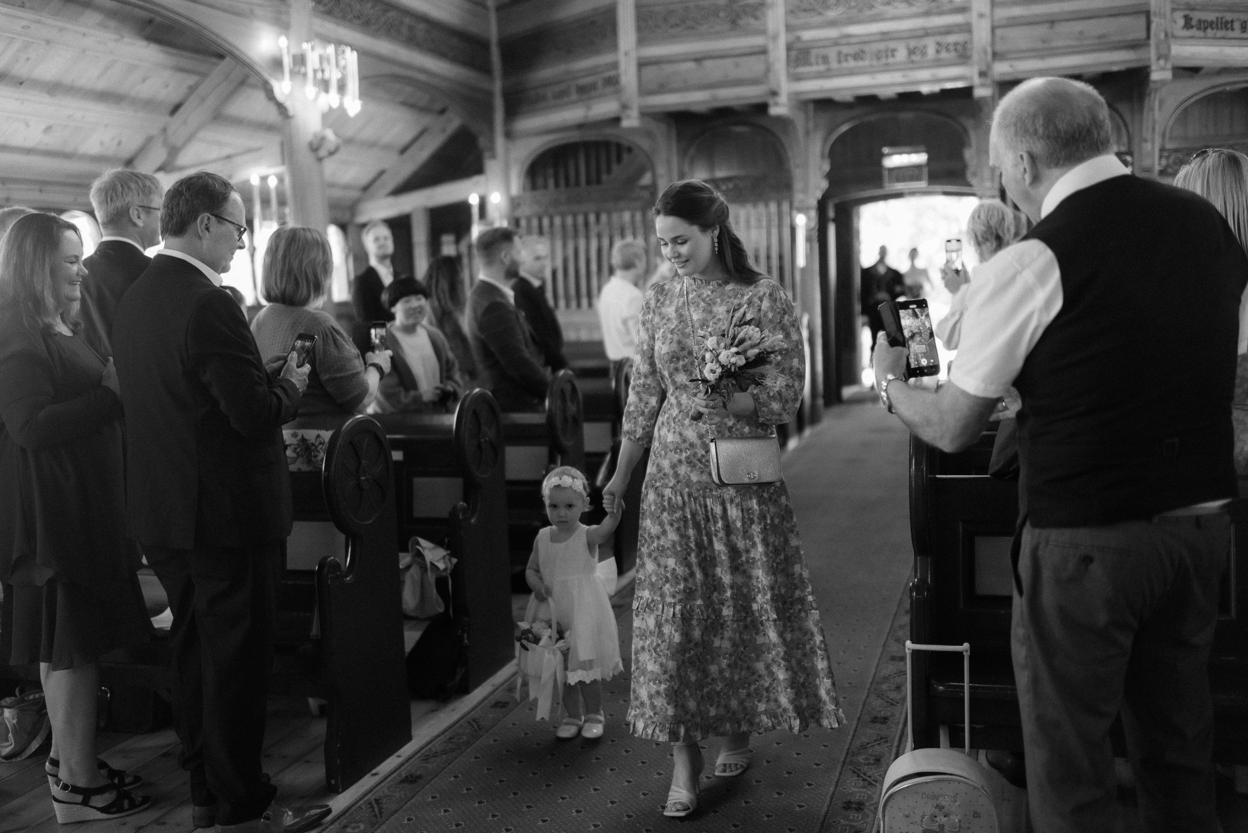 Black and white photo of people gathering inside a rustic wooden church hall.
