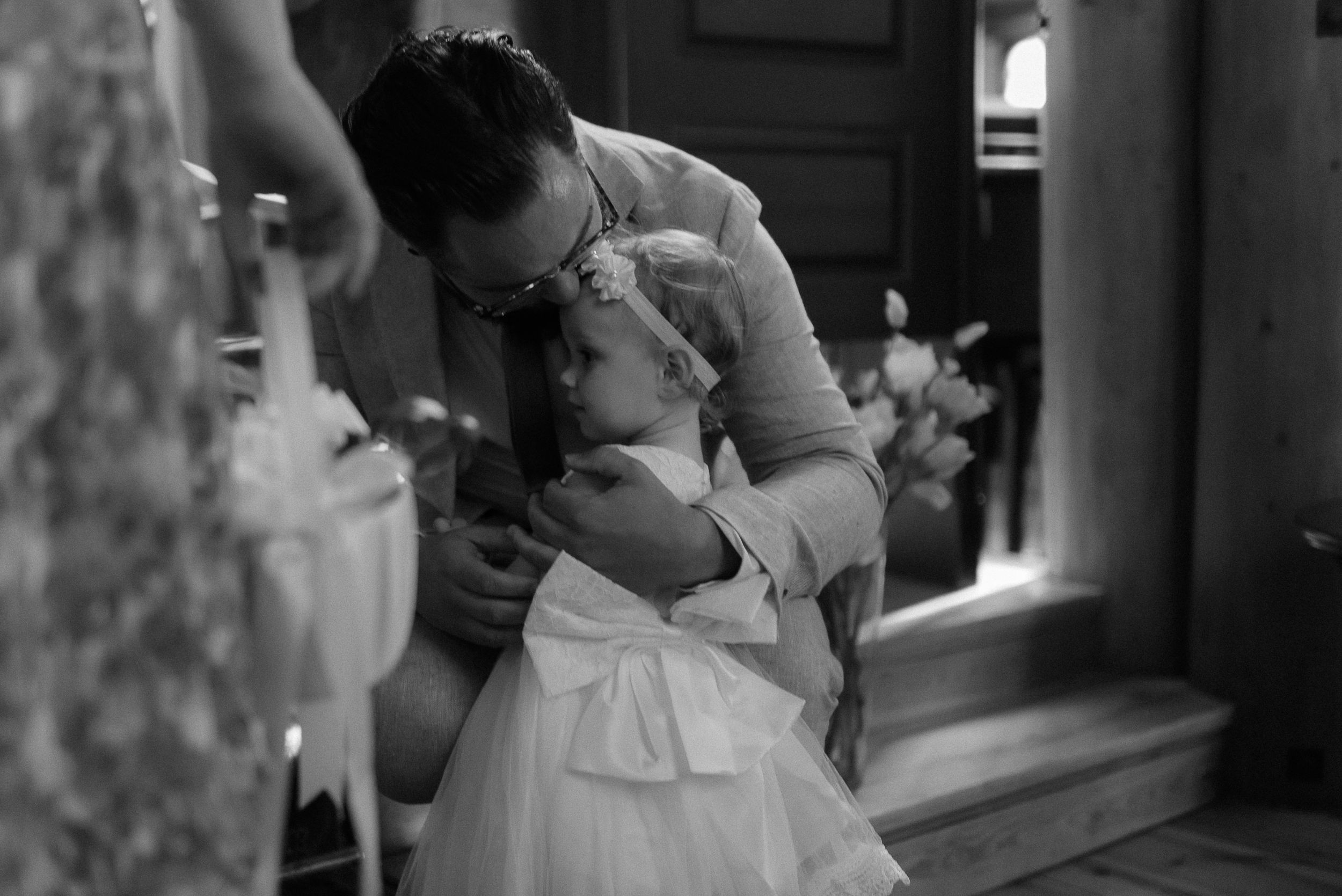 A tender black and white moment showing an adult adjusting a child's formal white dress.