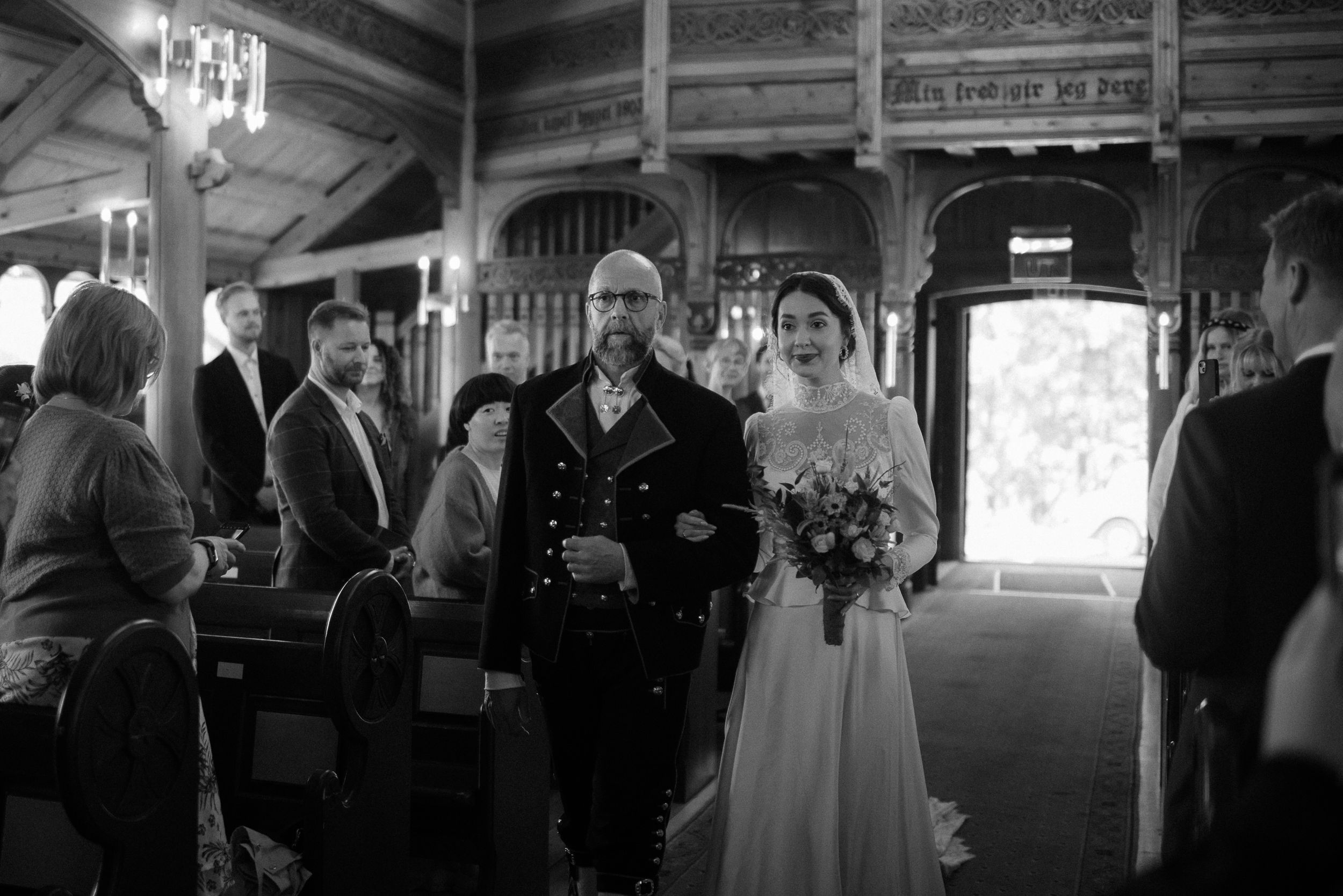 A classic black and white wedding ceremony scene in a rustic wooden venue with hanging chandeliers.