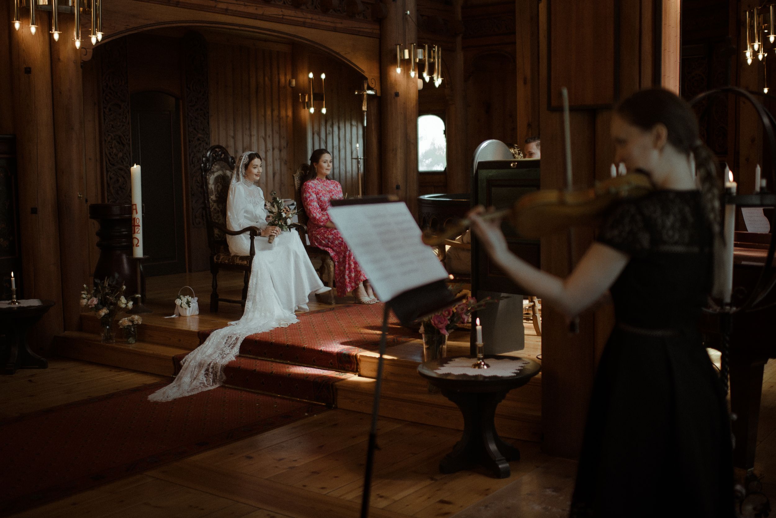 Musicians perform at a wedding ceremony in an elegant wood-paneled venue with hanging lights.