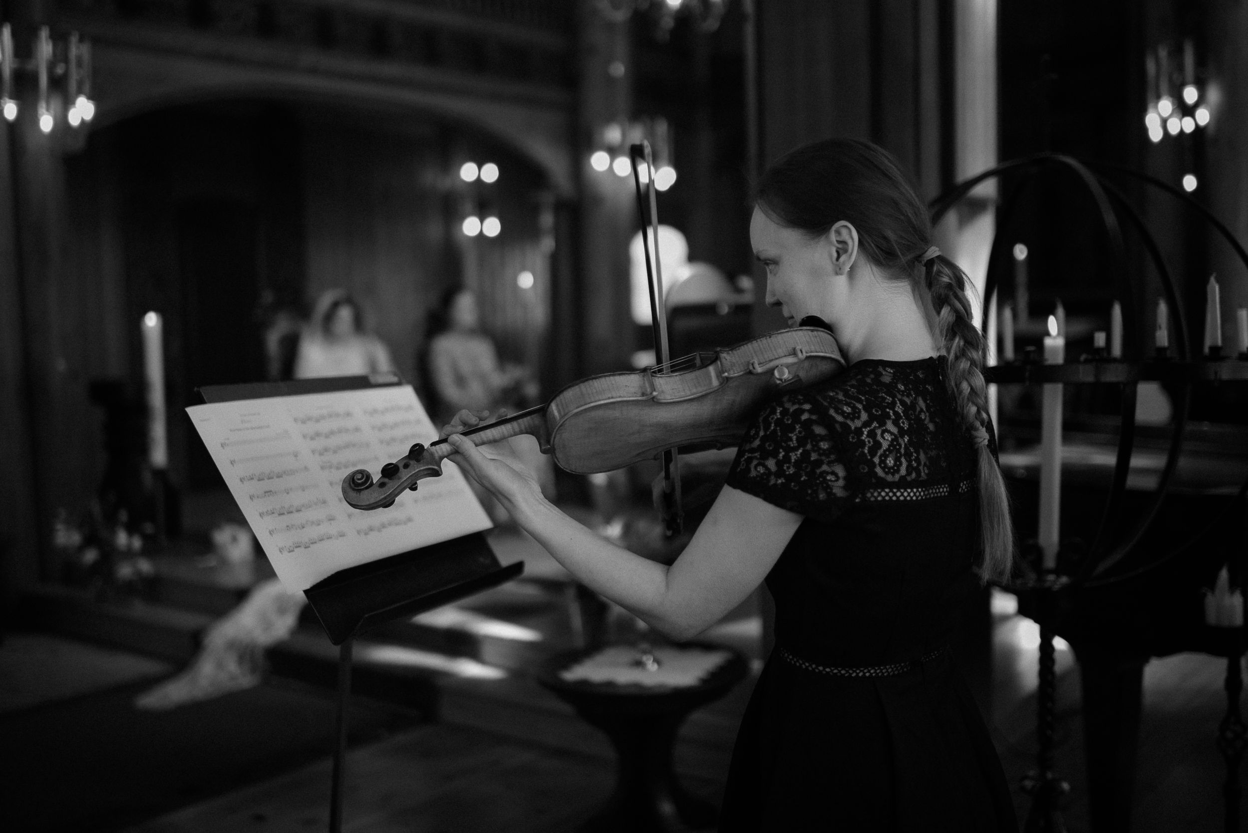 Musician in black dress playing violin during a dimly lit performance.