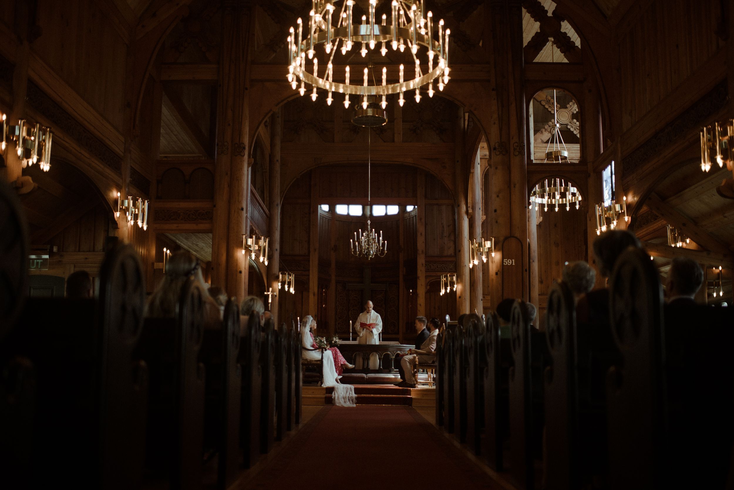 A dramatic church interior with glowing chandeliers and wooden pews leading to the altar.