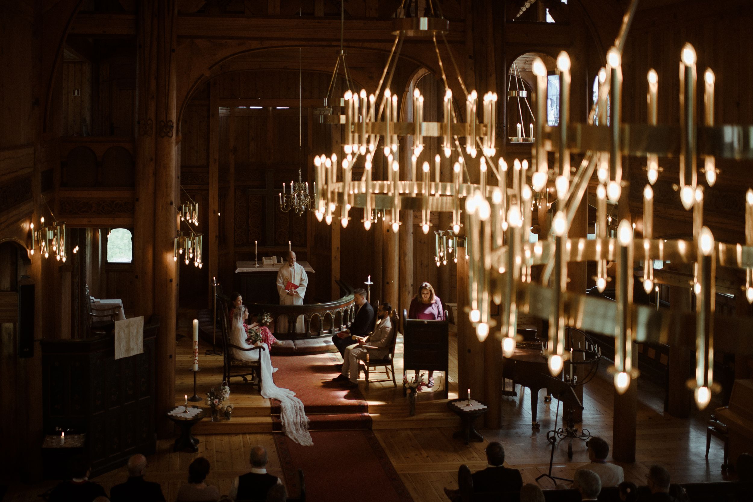 An atmospheric church interior illuminated by multiple hanging chandeliers and candles.