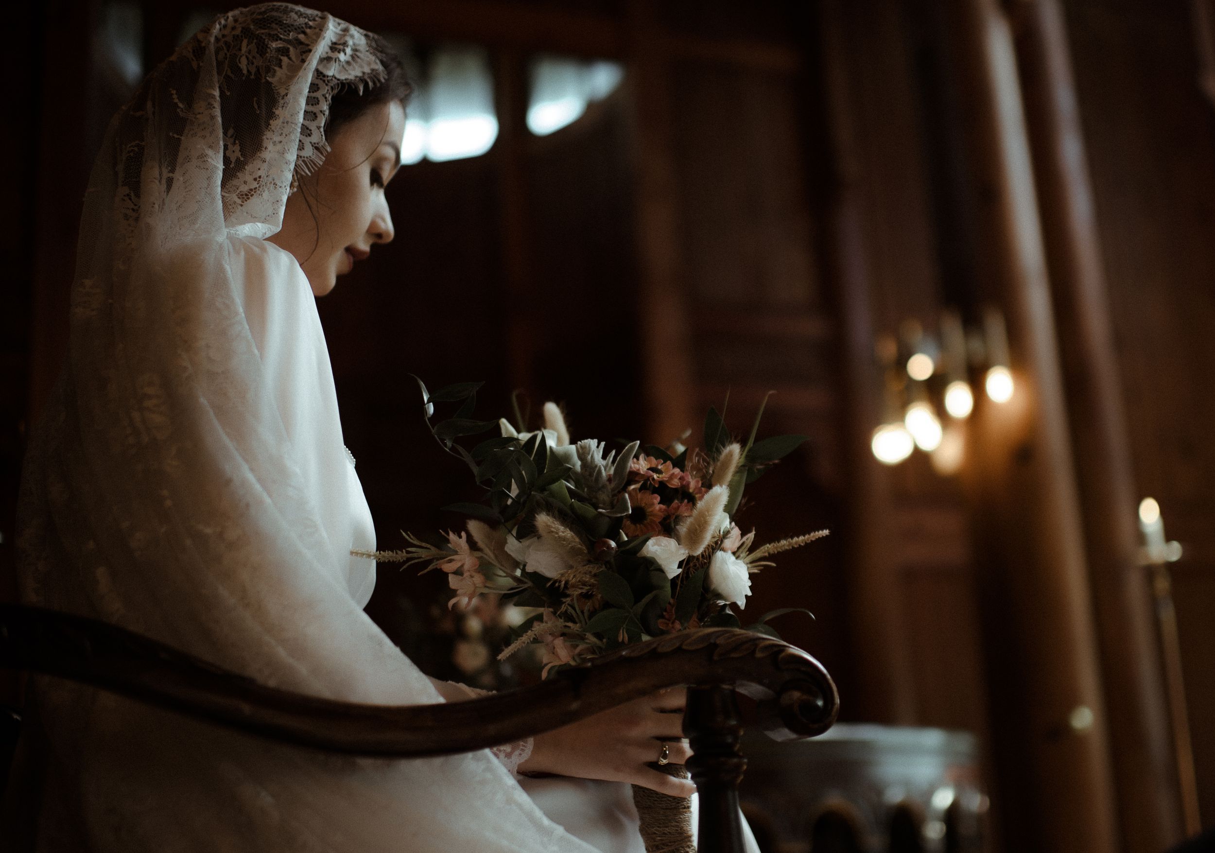 A moody side profile of a bride holding a bouquet in a beautifully lit church setting.