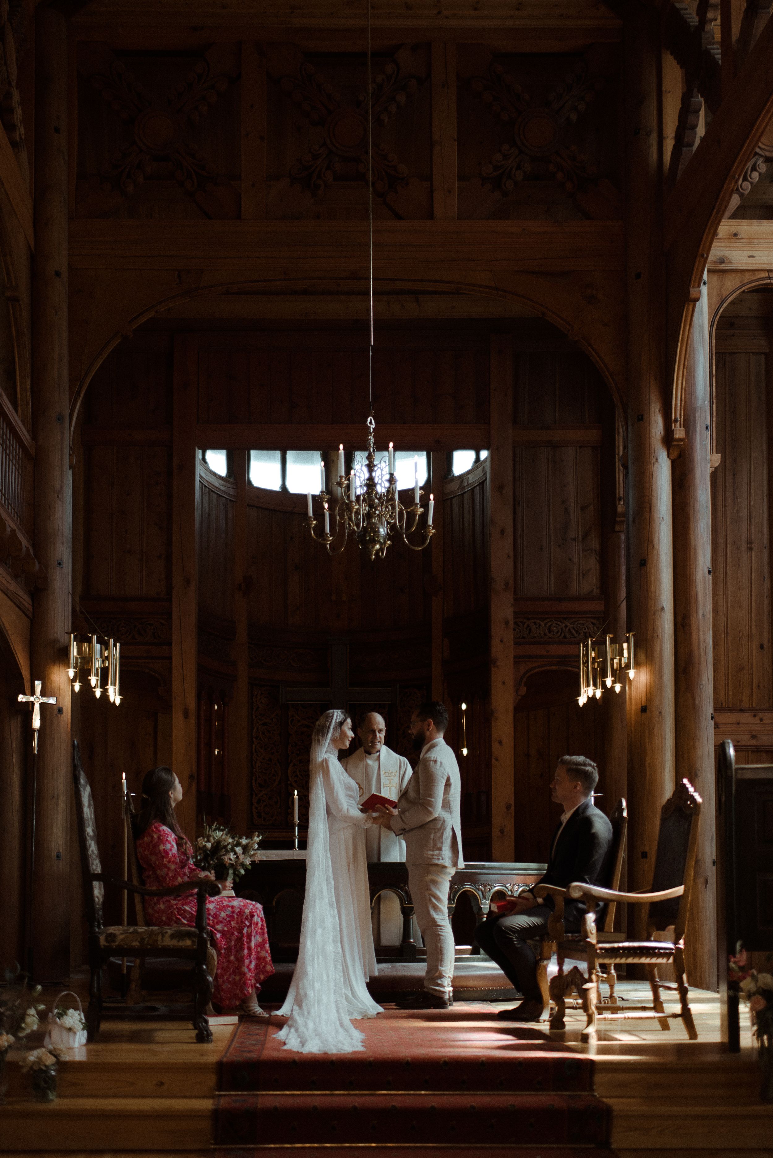 An intimate wedding ceremony takes place in an elegant wood-paneled chapel under a crystal chandelier.