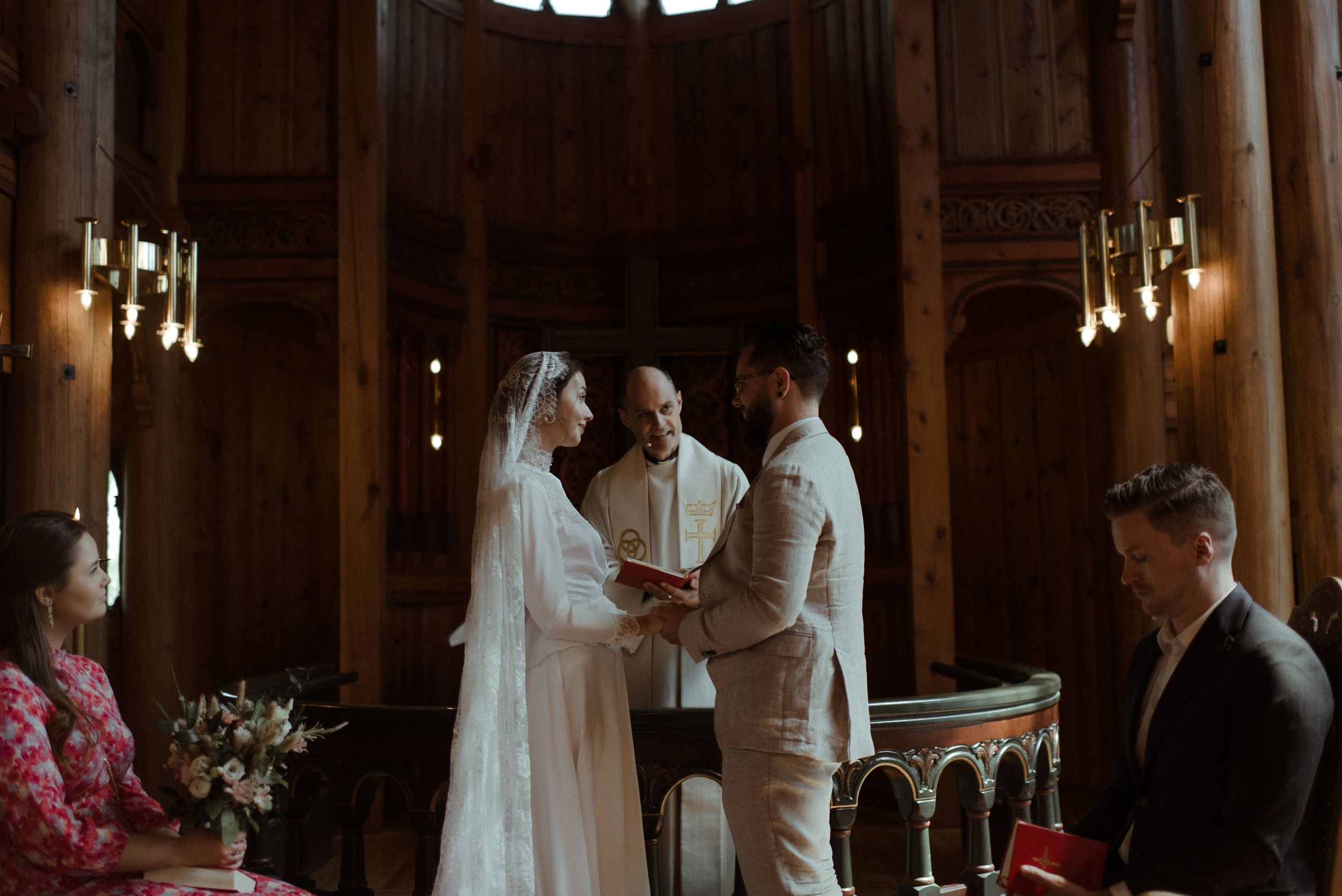 A wedding ceremony unfolds in a historic chapel with warm lighting and wooden architectural details.