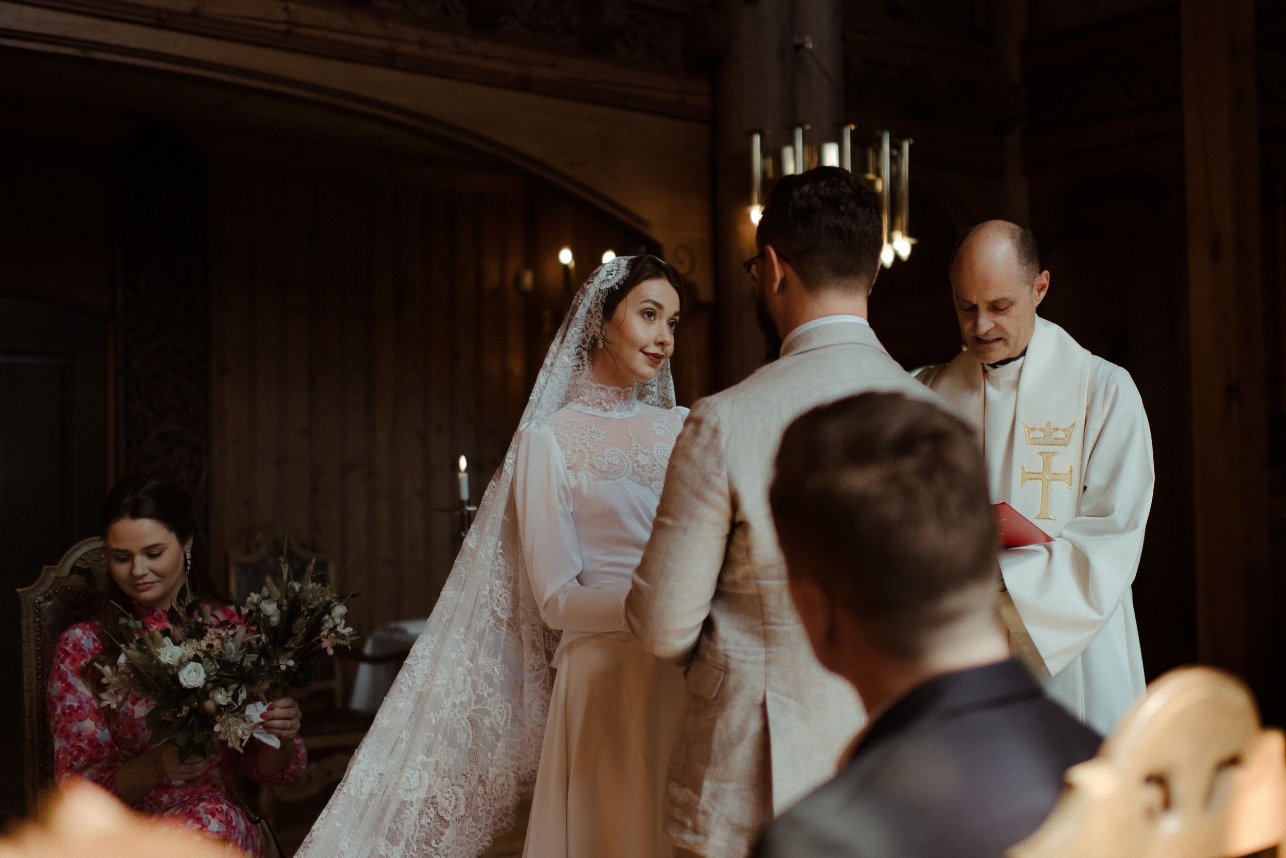 An intimate wedding service in progress within a grand wooden chapel with ornate light fixtures.