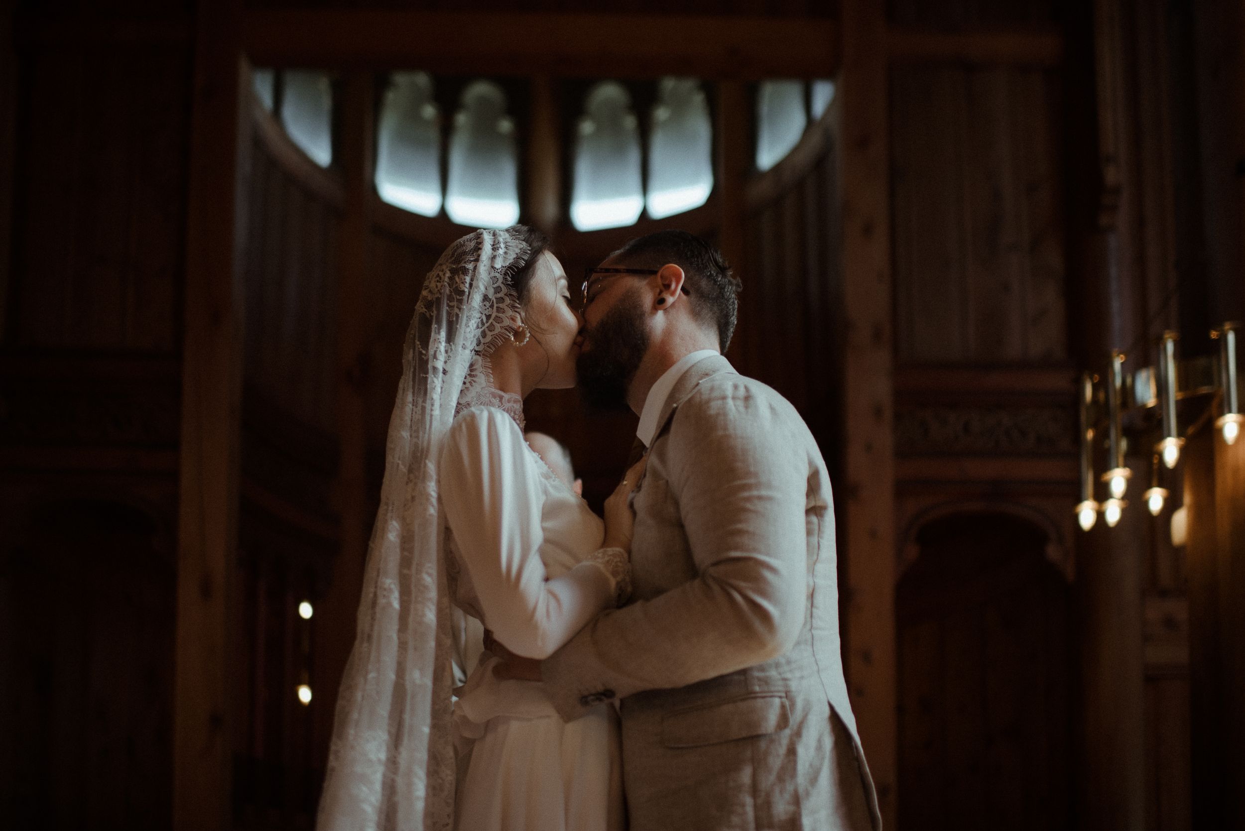 A tender wedding moment captured in moody lighting beneath arched chapel windows.