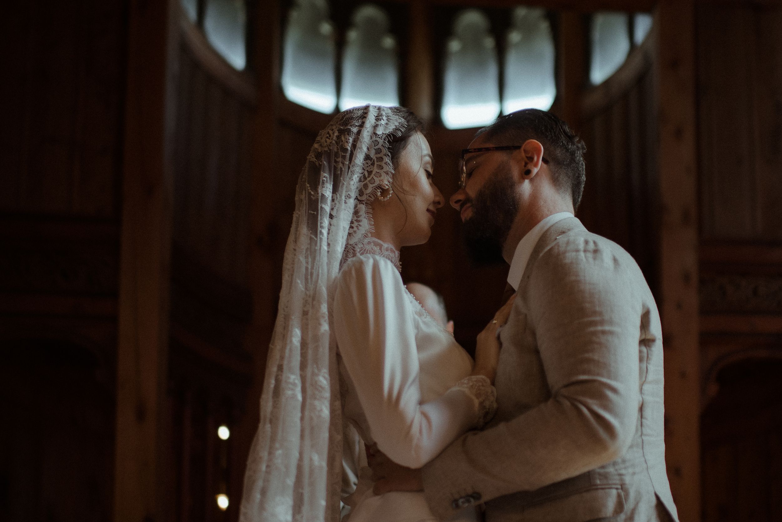 An intimate wedding portrait in a chapel with dramatic backlighting and Gothic architectural elements.