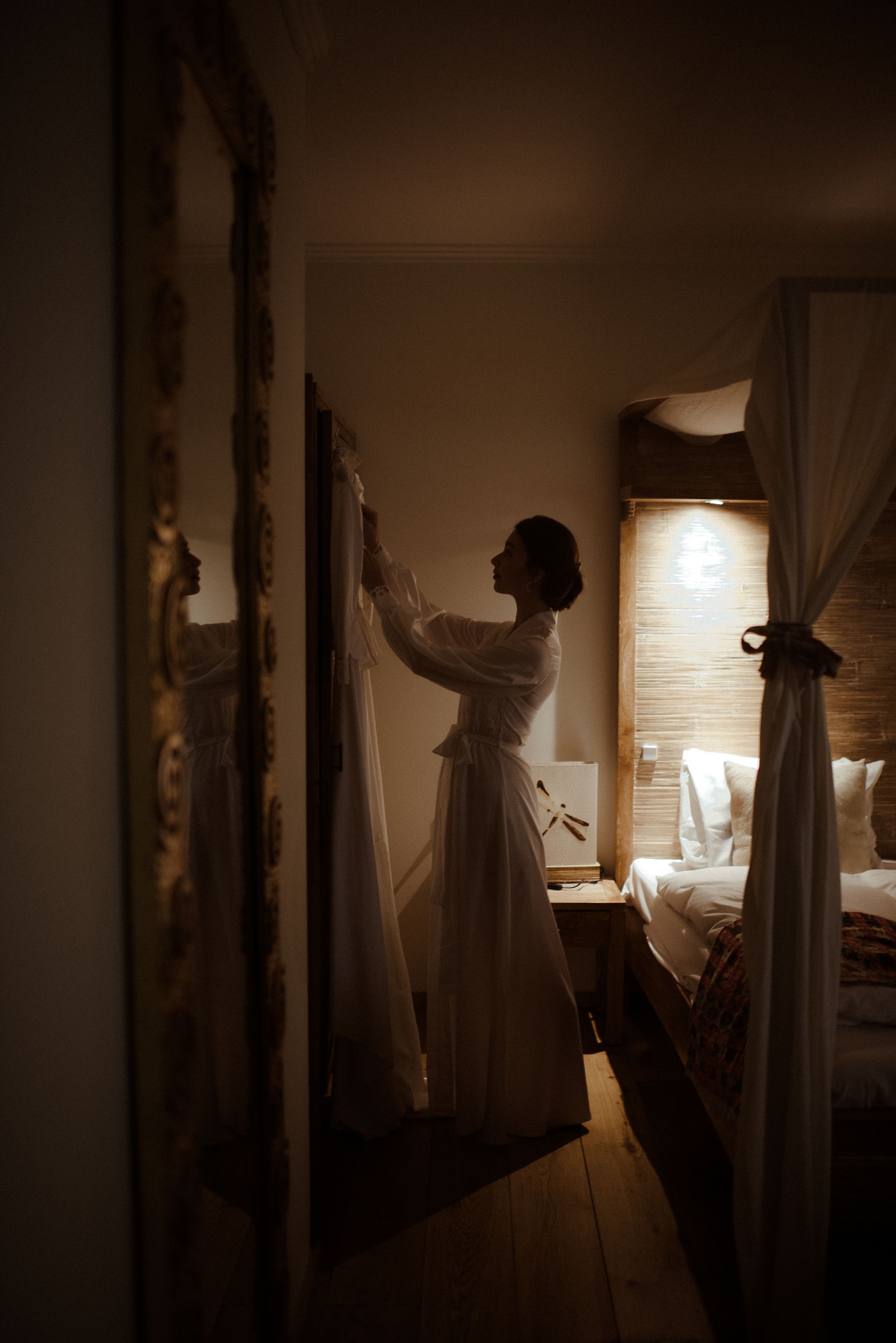 Silhouette of figure in vintage dress reaching up in a warmly lit room.